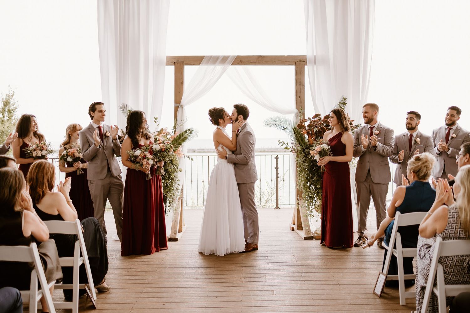 Wedding ceremony setup with white draping and wooden arch at waterfront venue.