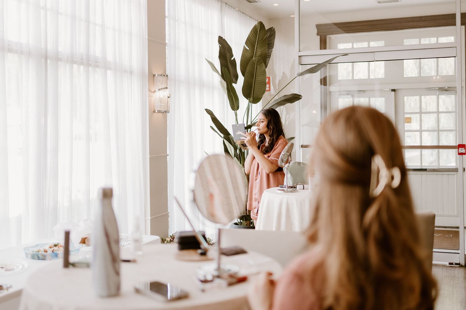 Bright bridal preparation room with large windows and elegant table settings.