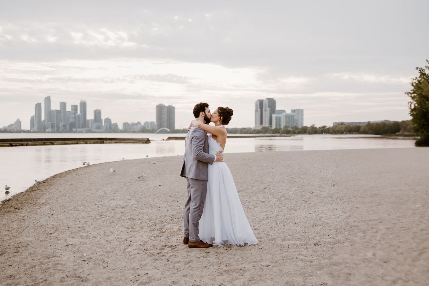 Wedding couple shares intimate moments on a sandy beach with downtown buildings visible in the distance.