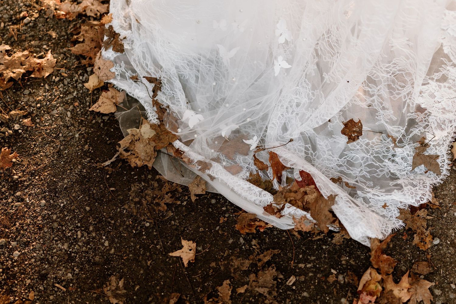 White wedding dress train trailing over fallen autumn leaves on the ground.