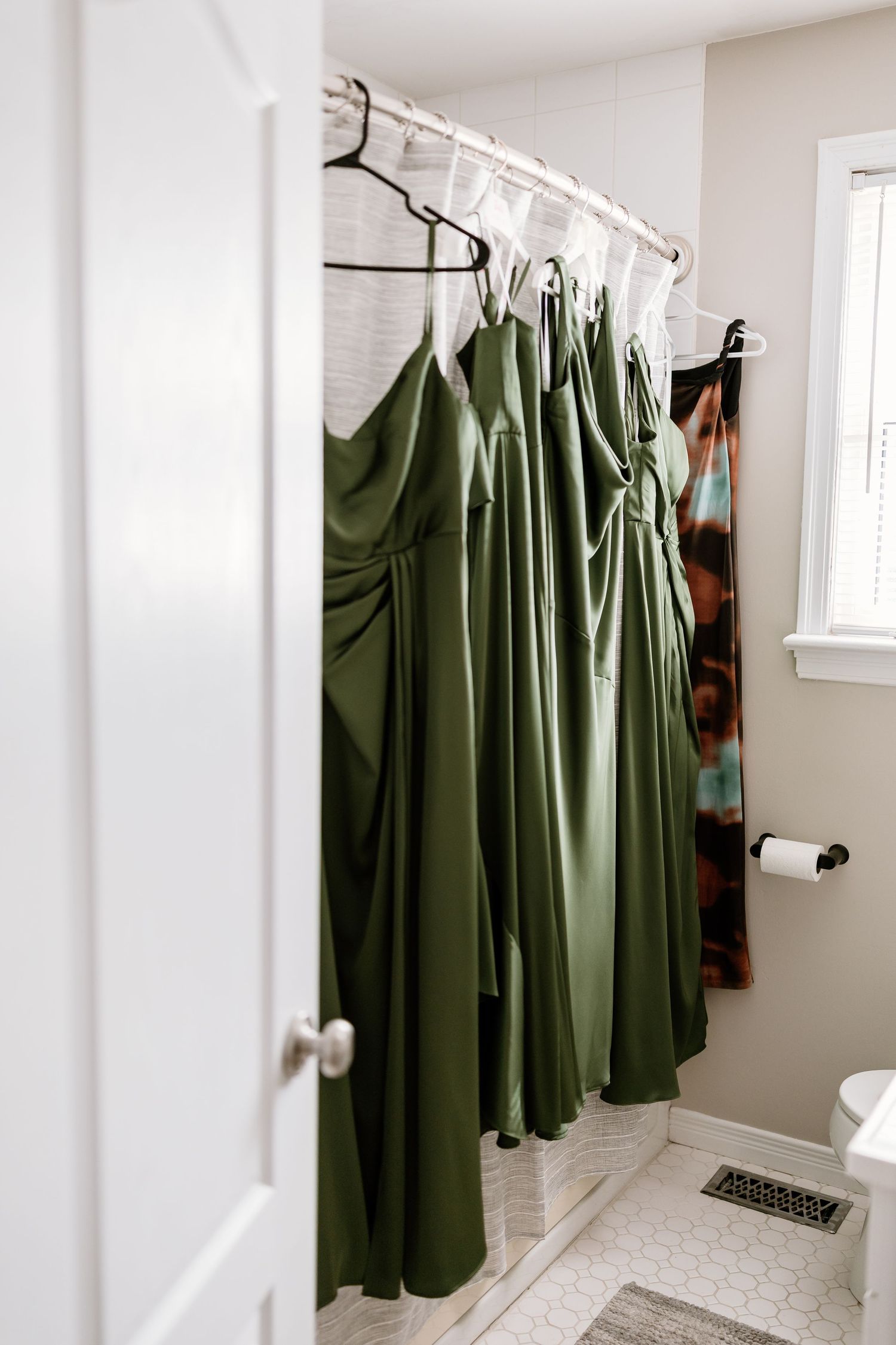 A row of sage green bridesmaid dresses hanging in a bright dressing room.