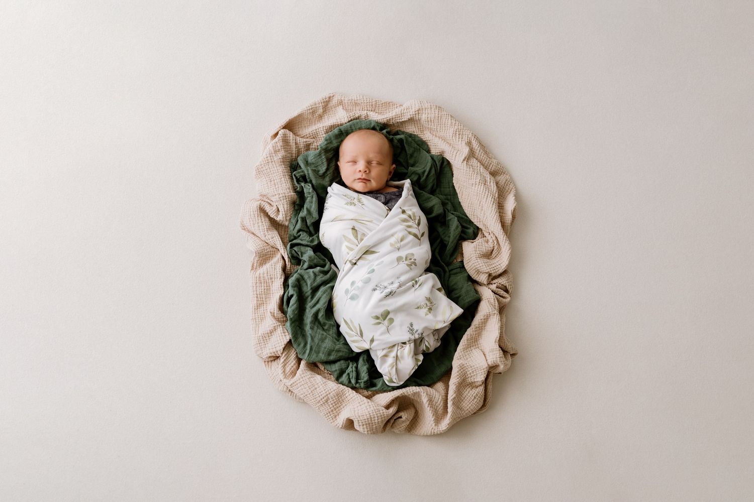 Newborn baby sleeping peacefully in circular nest of soft neutral fabrics.