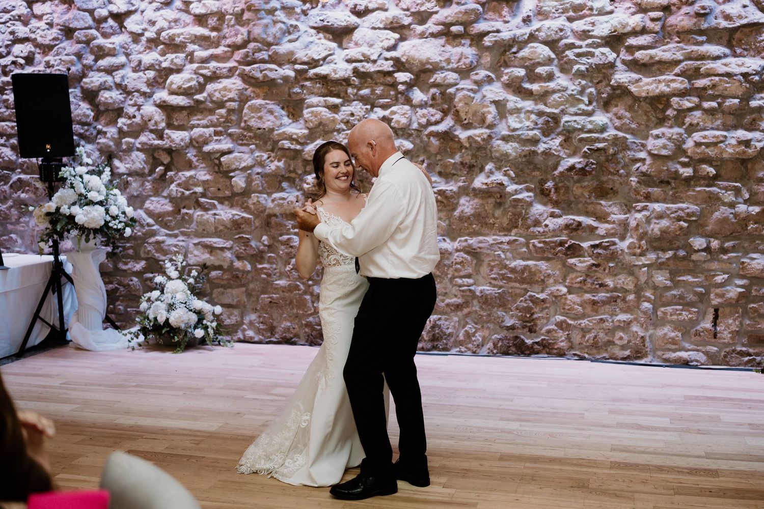 Wedding reception guests dancing together in an elegant venue with stone walls and romantic lighting.