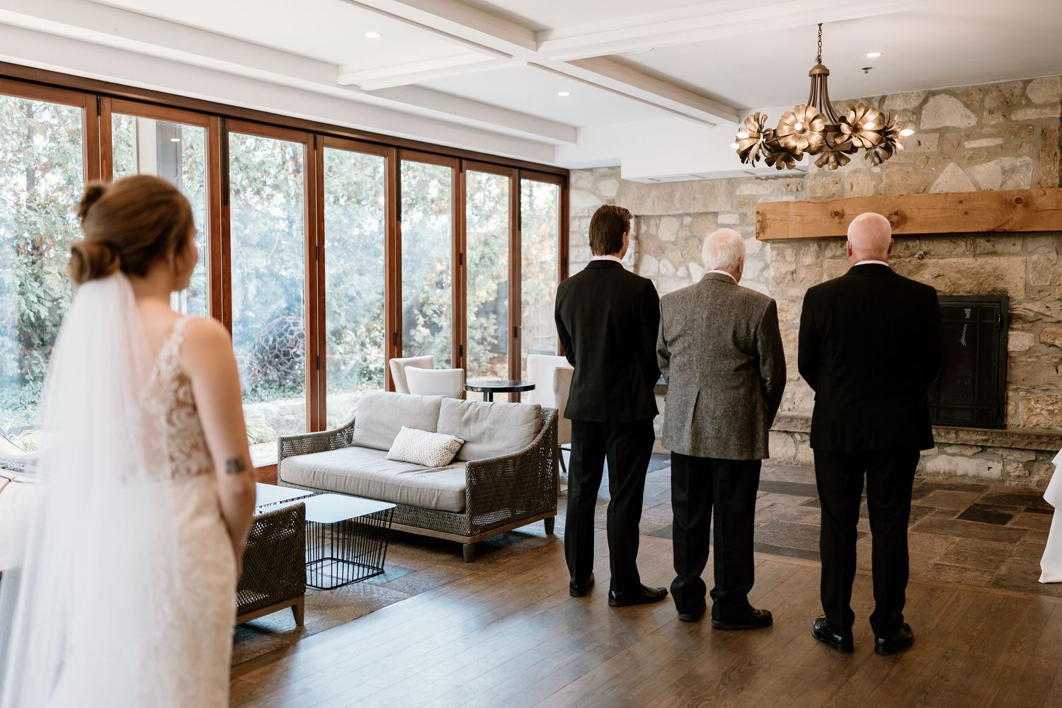 Three people stand facing large windows in an elegant room with stone walls.