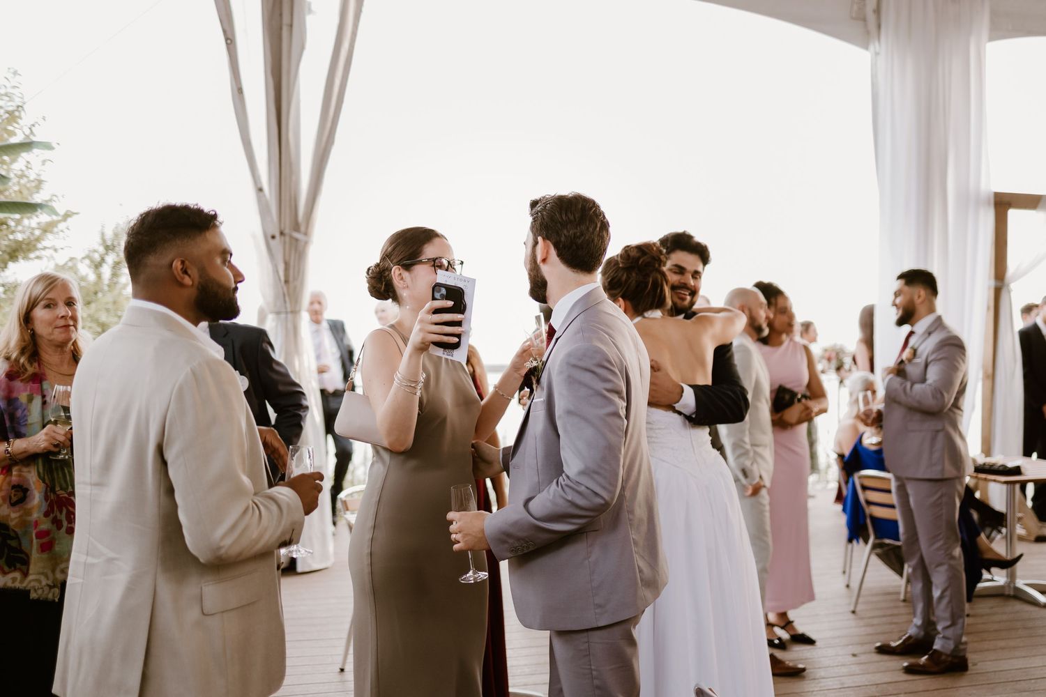 Wedding reception guests mingle and celebrate in an elegant white-draped indoor venue.