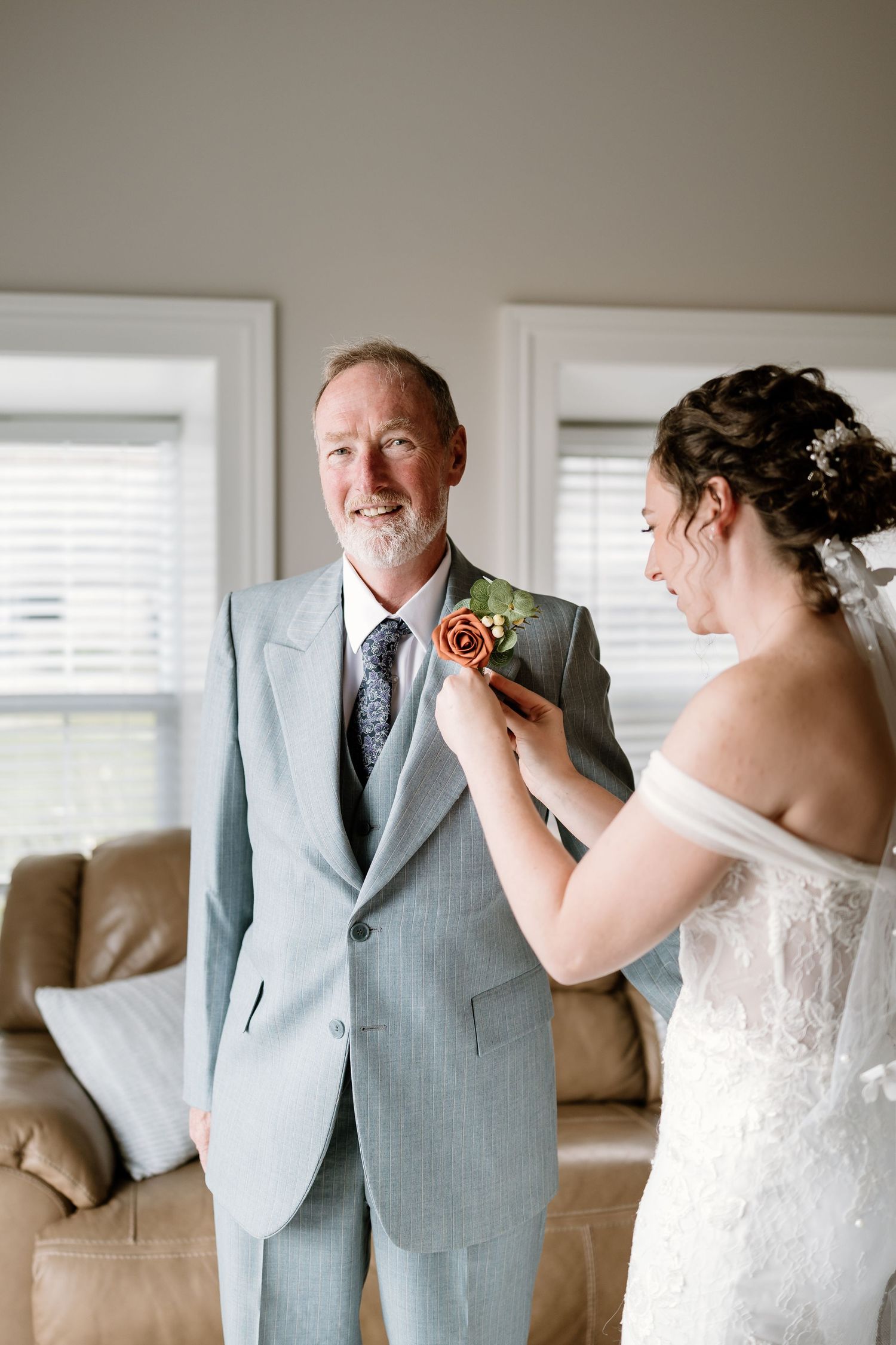 A sweet interaction showing a boutonniere being pinned on a light gray suit jacket.