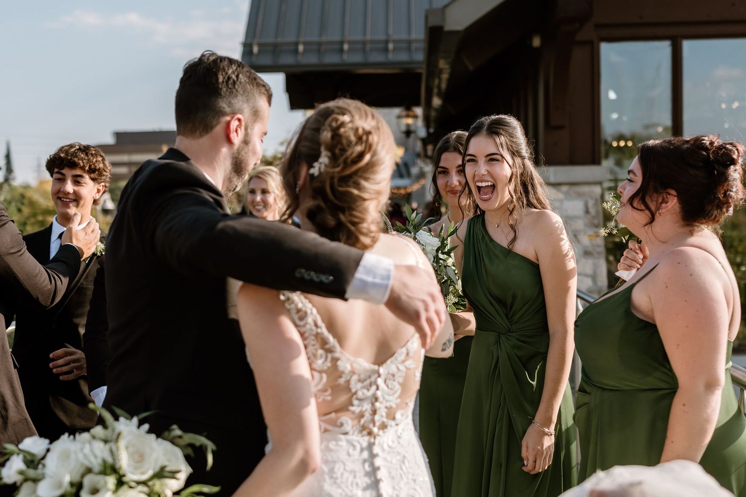 Joyful wedding party celebrates together on a sunny outdoor balcony.