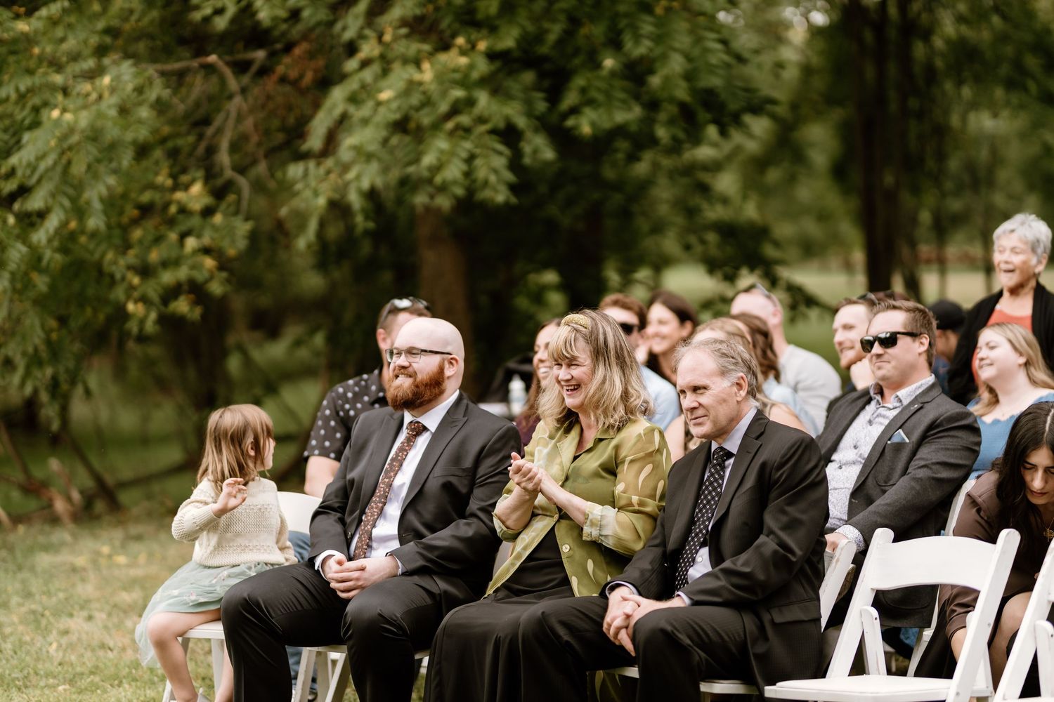 Wedding guests seated outdoors for ceremony in natural garden setting.