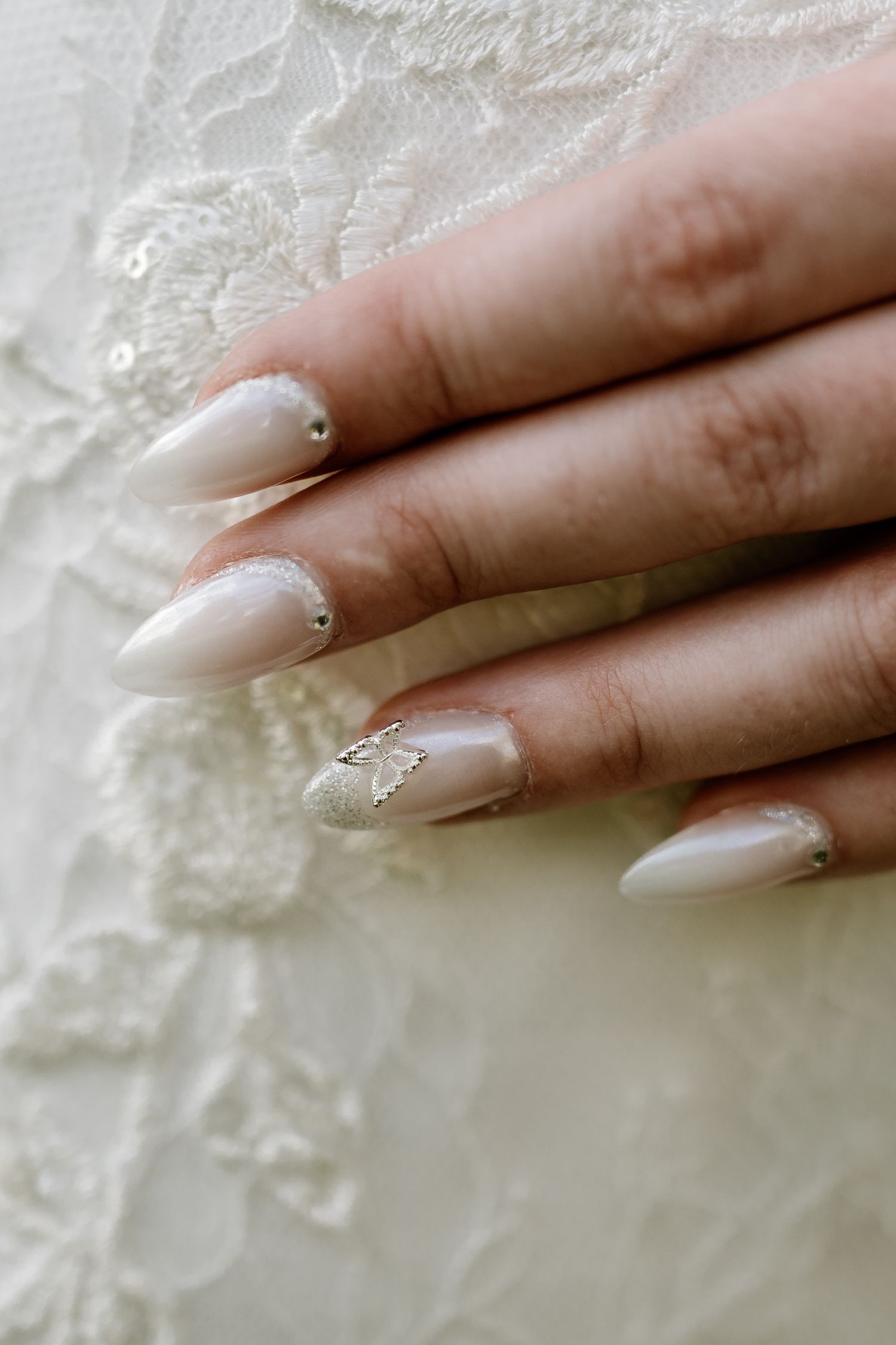 Elegant bridal manicure with long almond-shaped nails against white lace fabric.
