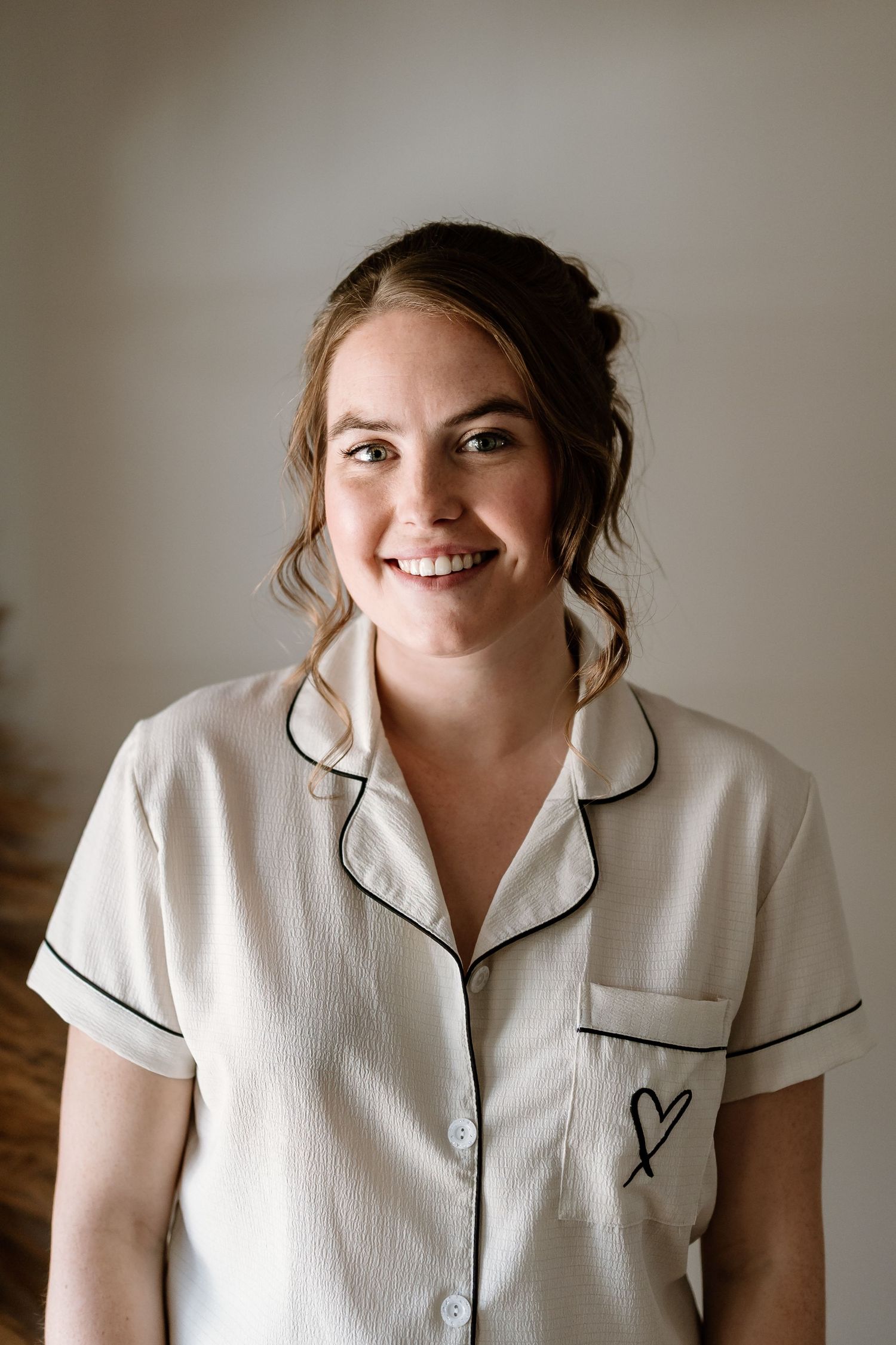 Woman wearing white pajama-style top with black piping and embroidered heart detail smiles at camera.