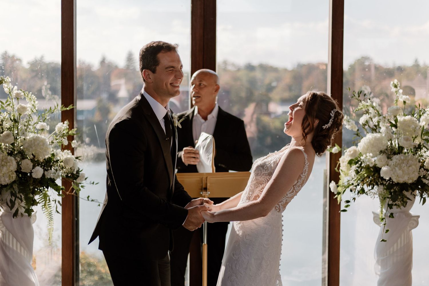 Wedding ceremony with white floral arrangements framing the couple against scenic window backdrop.