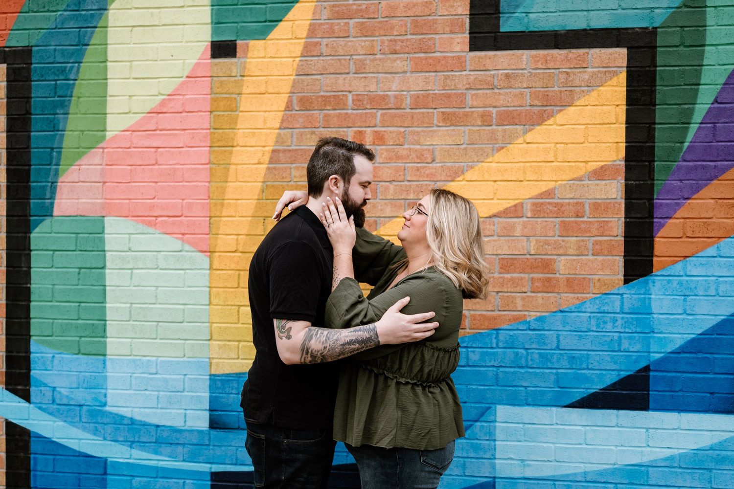 Couple sharing a romantic moment in front of a colorful street mural, man with tattoos embracing woman.