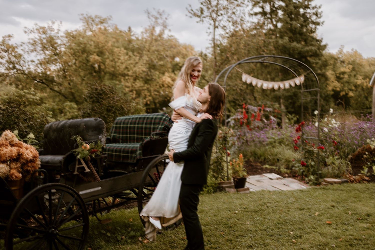 Romantic wedding moment captured in garden setting with vintage car and floral arch.