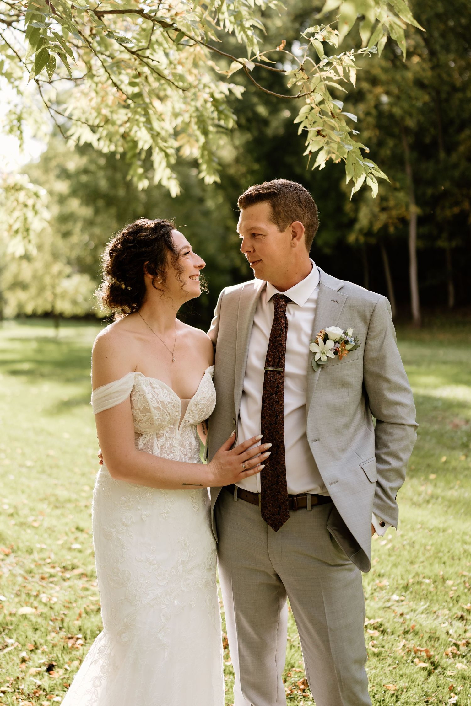 A romantic wedding portrait captured in golden sunlight beneath overhanging tree branches.
