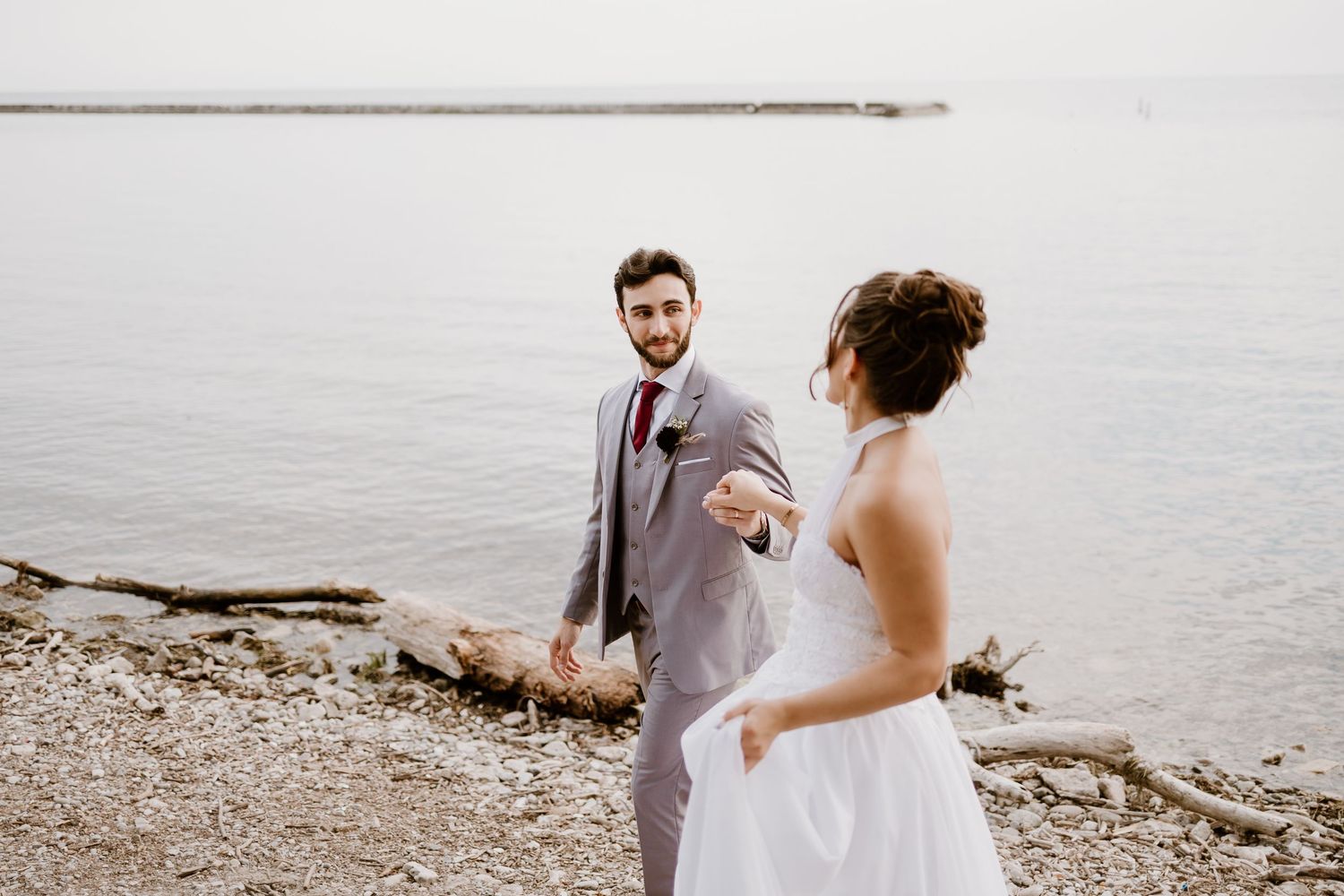 A lighthearted exchange between a bride and groom on a rocky shoreline.