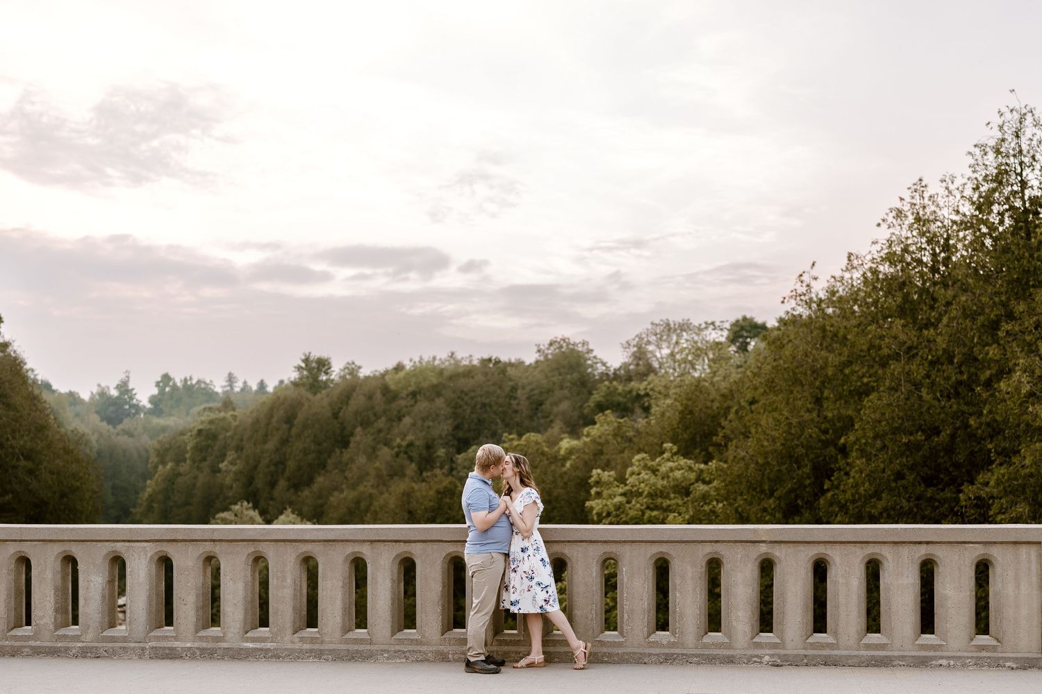 A couple sits together on a bridge railing during sunset.