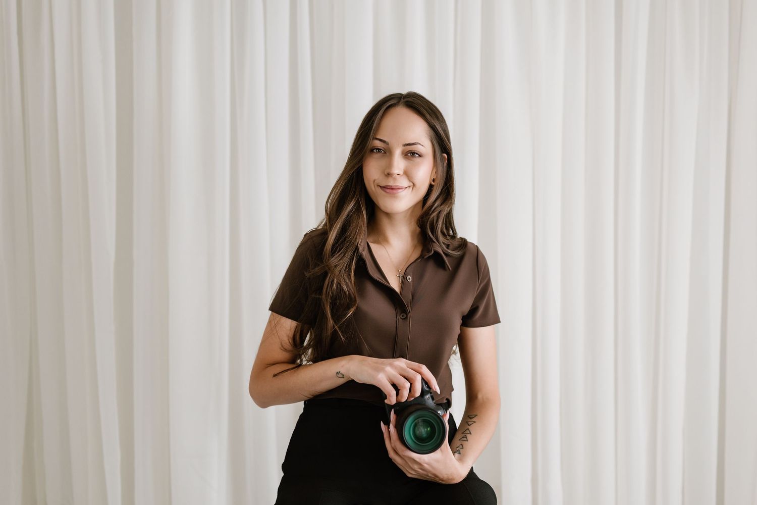 Person in a brown dress standing against a white curtain background.