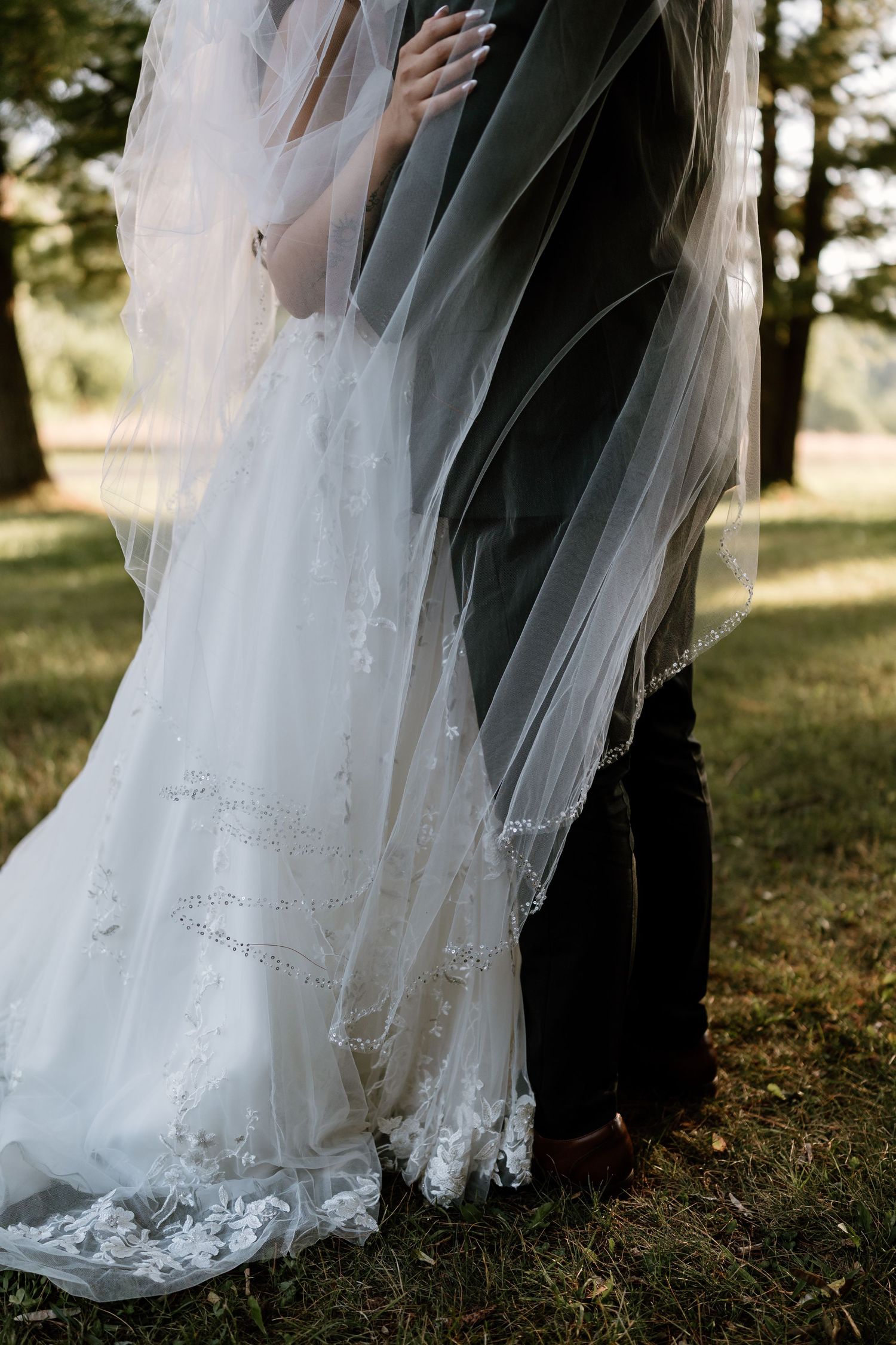Close-up of bride in lace wedding dress and groom embraced under a billowing veil outdoors.