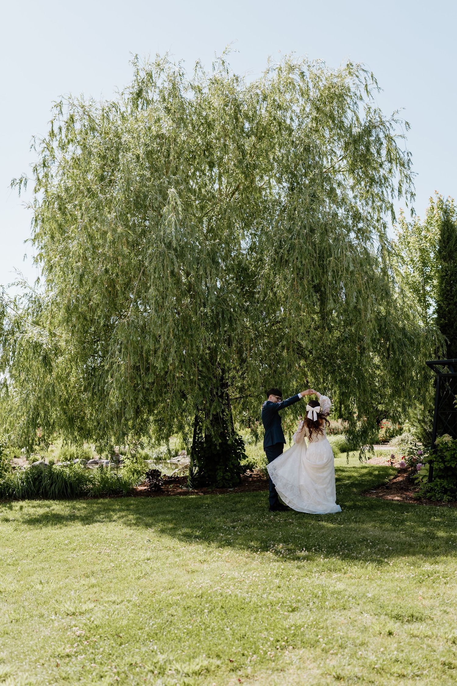 Bride and groom dancing under a large weeping willow tree on a sunny day.