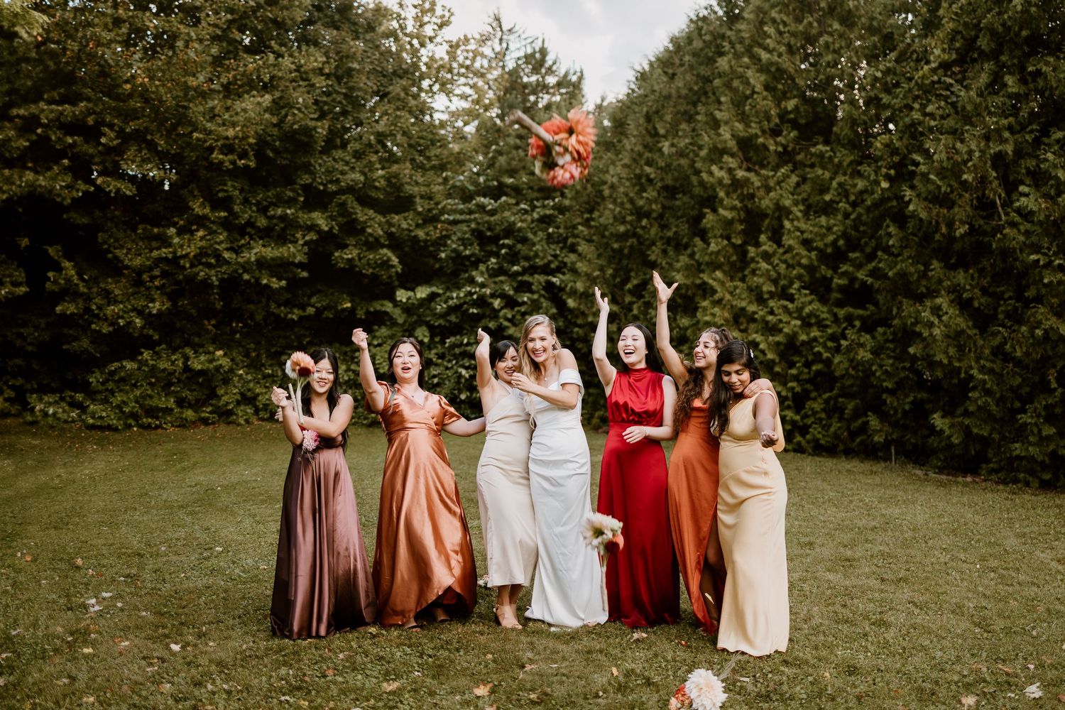 Wedding party celebrates on a green lawn by tossing flower petals in the air.