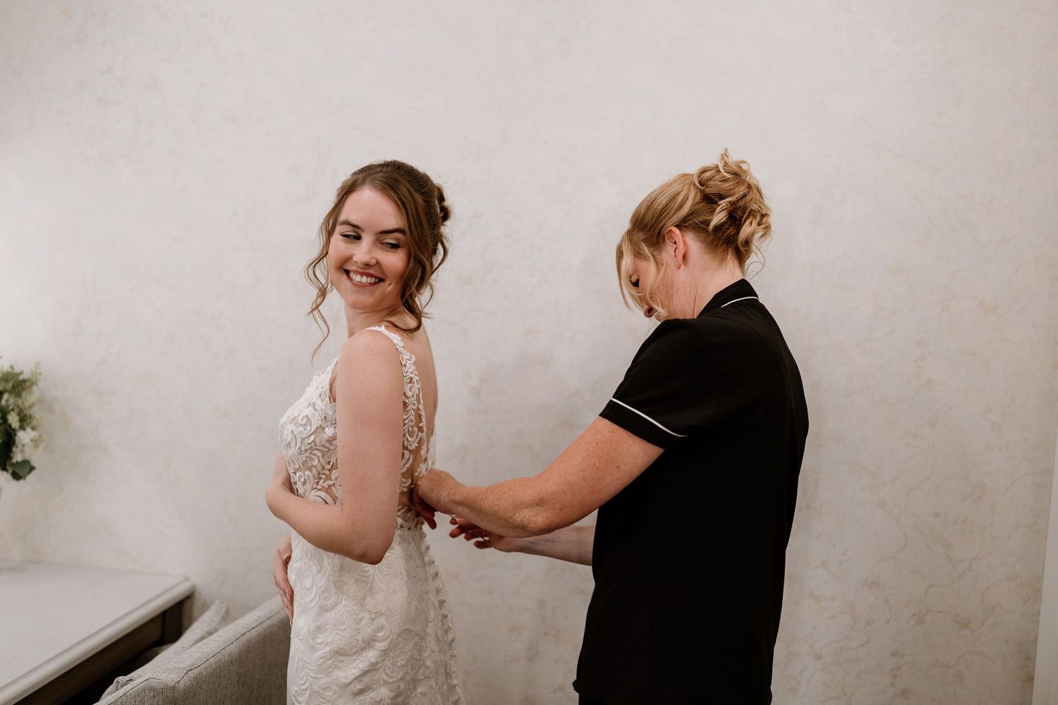 Getting ready scene with a wedding dress being fitted in a bright room.