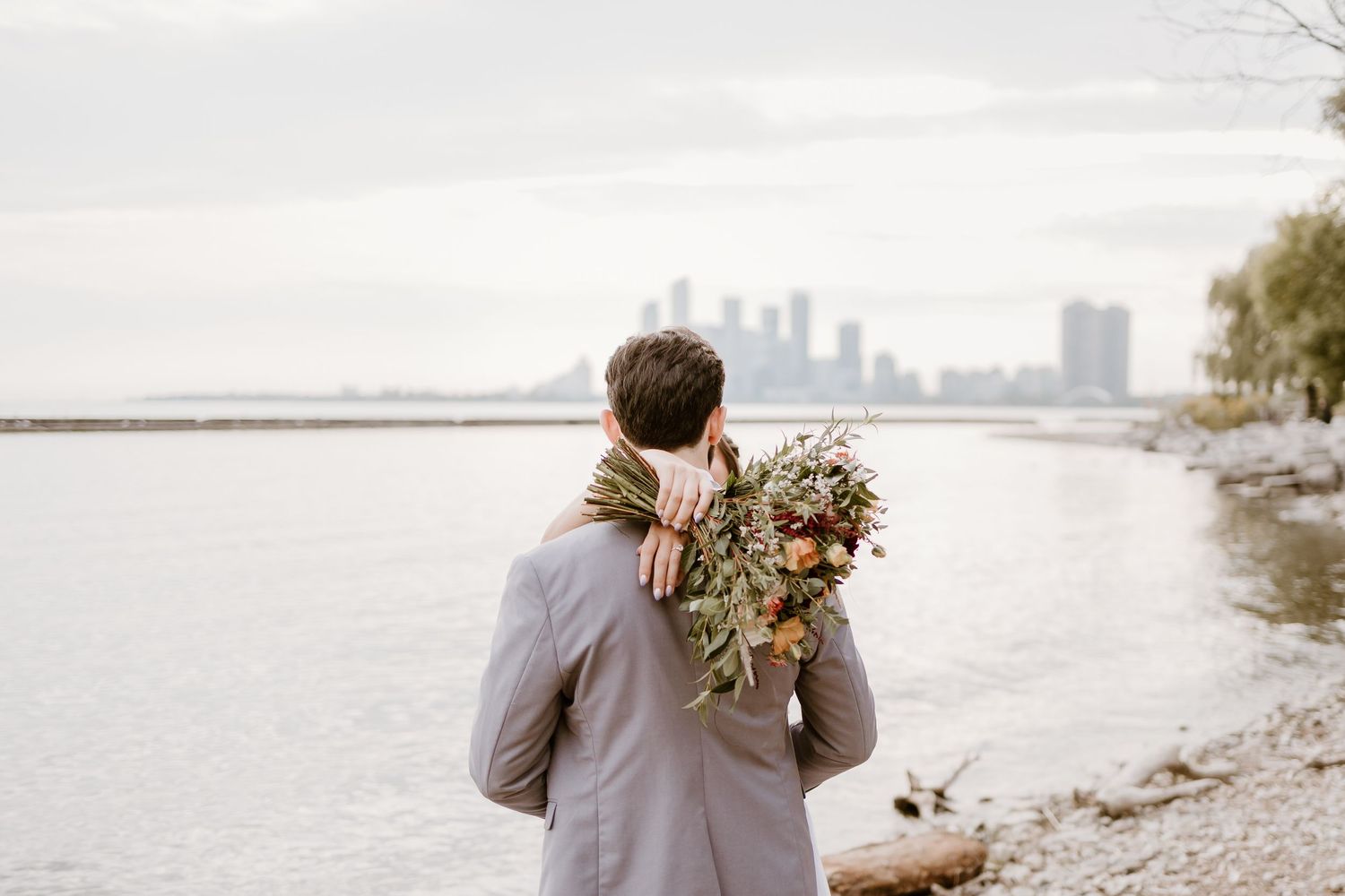 Couple walking along waterfront with city skyline in background.