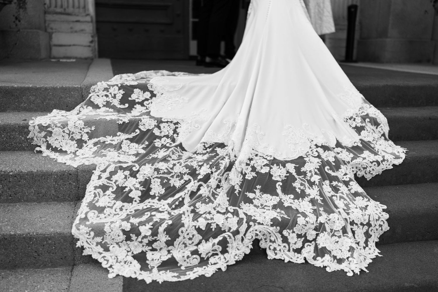 Ornate lace details of a wedding dress train spread across dark flooring.
