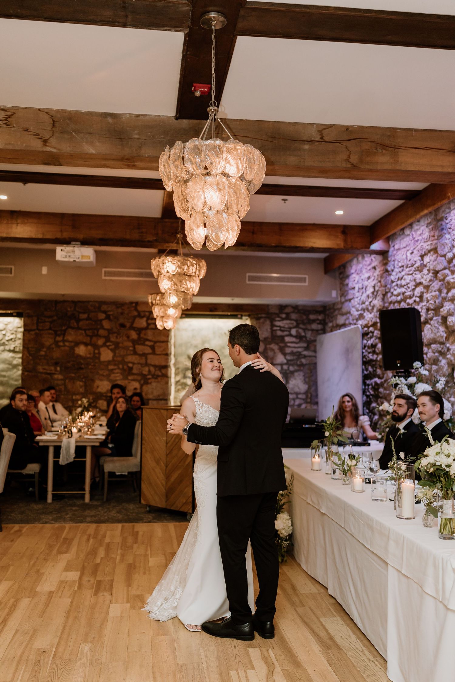First dance moment under crystal chandeliers in an elegant rustic reception venue.