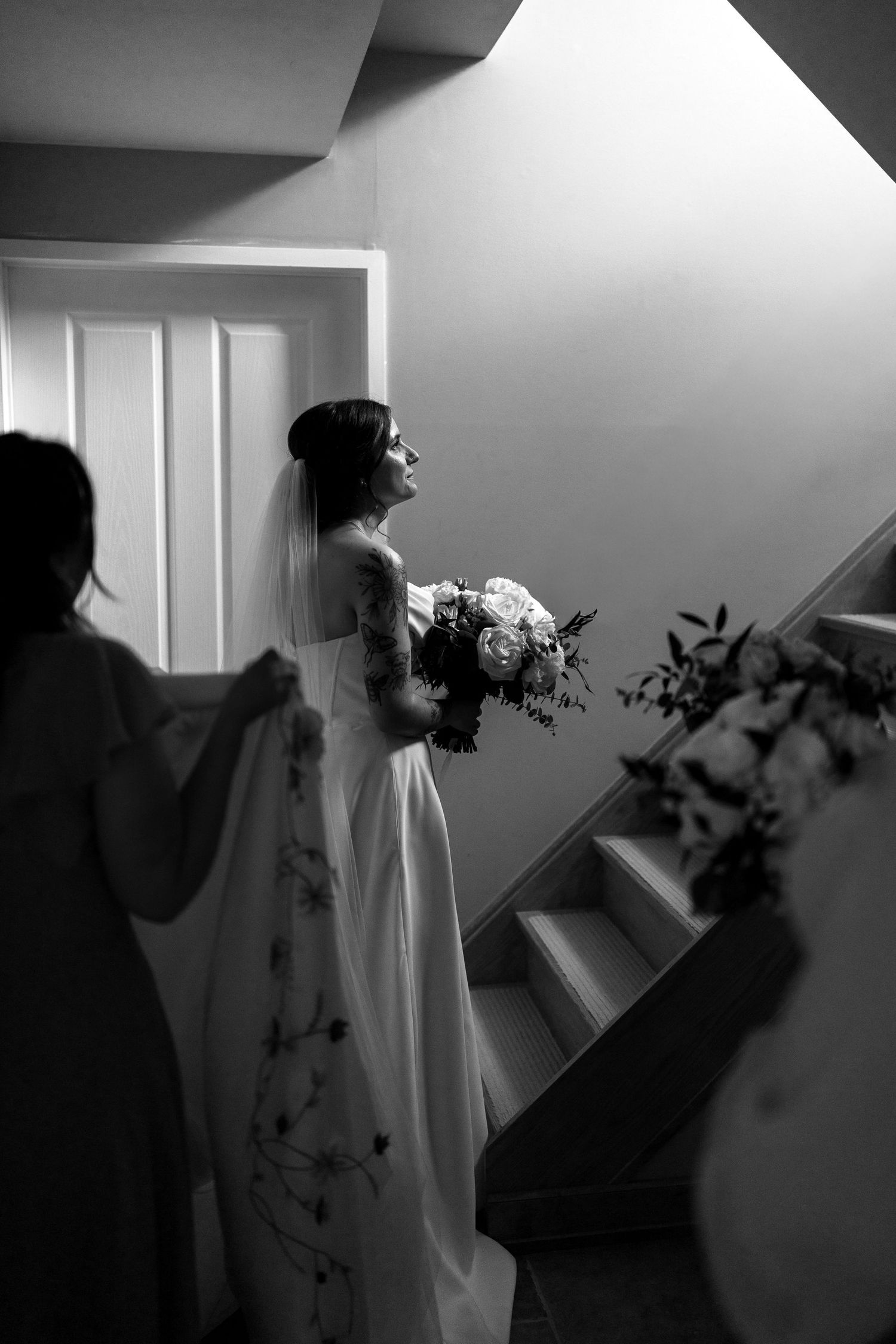 Artistic black and white photo of bride in wedding dress near window with dramatic shadows.