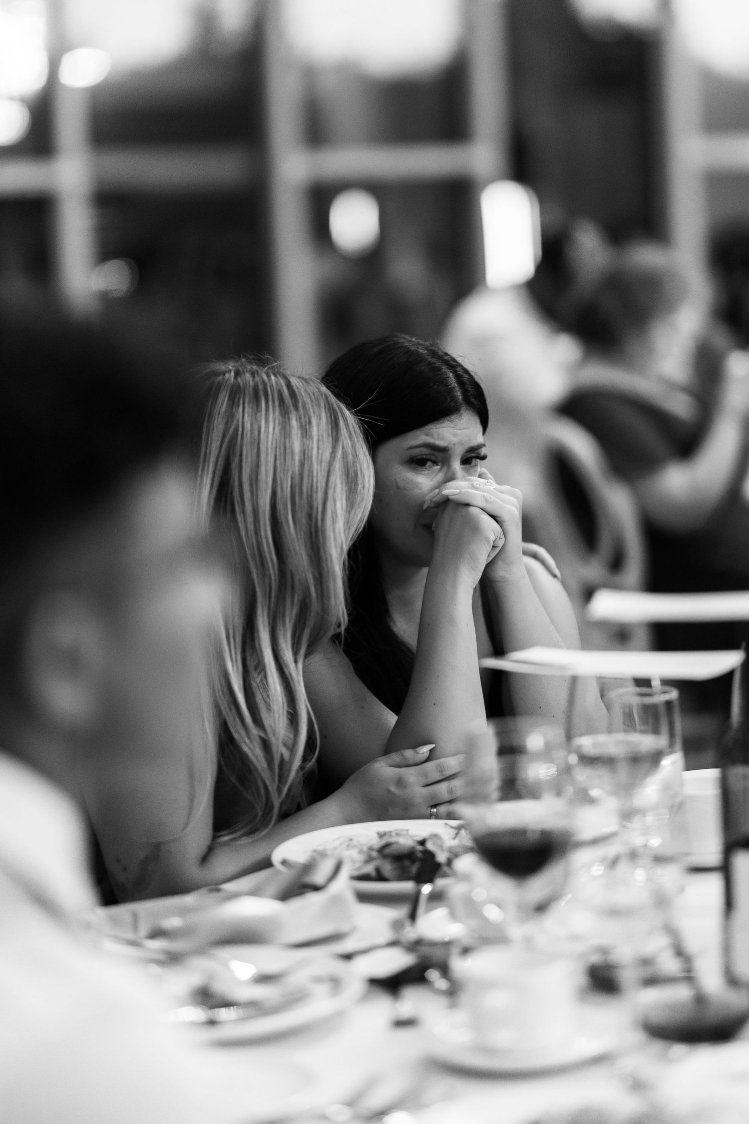 Black and white photo of two women sharing an intimate conversation at a wedding reception dinner table.