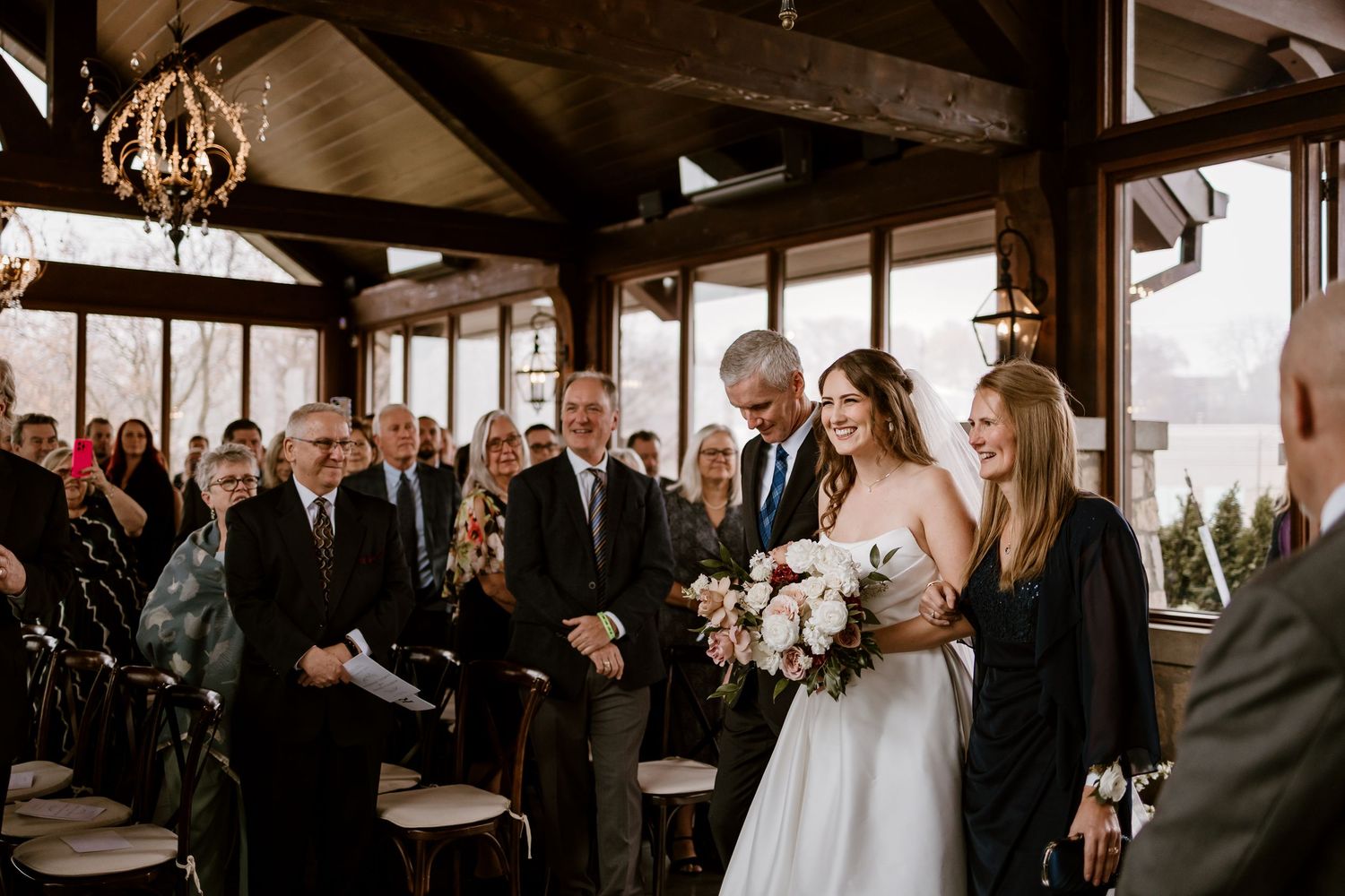 Wedding ceremony in progress inside a timber-framed venue with hanging chandeliers.