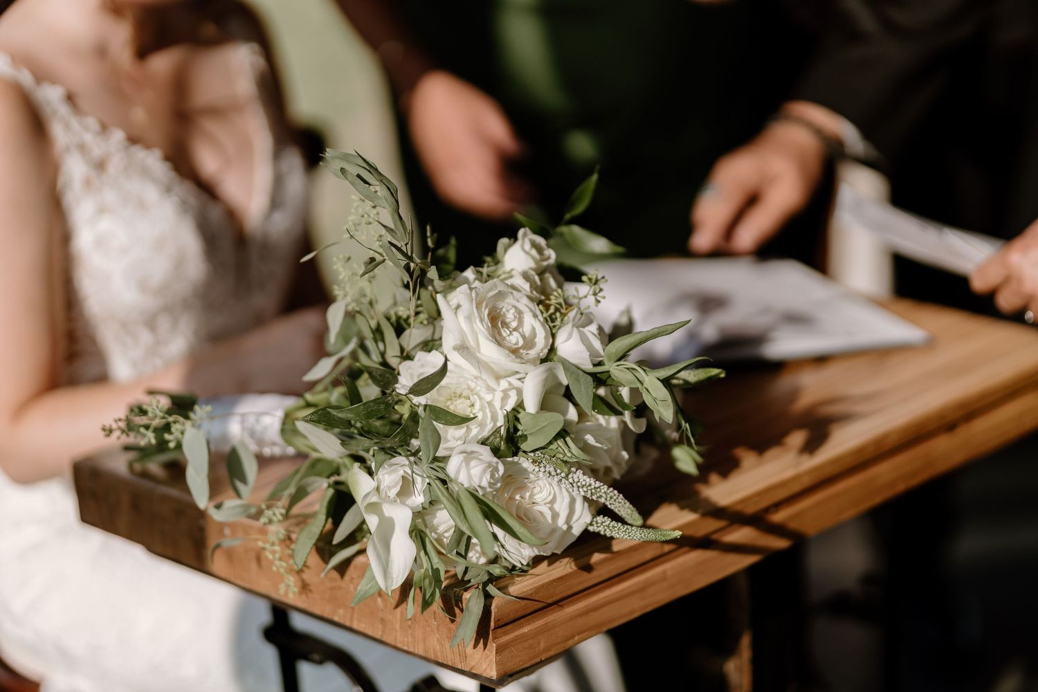 Wedding ceremony details with white floral arrangements and greenery on wooden stand.