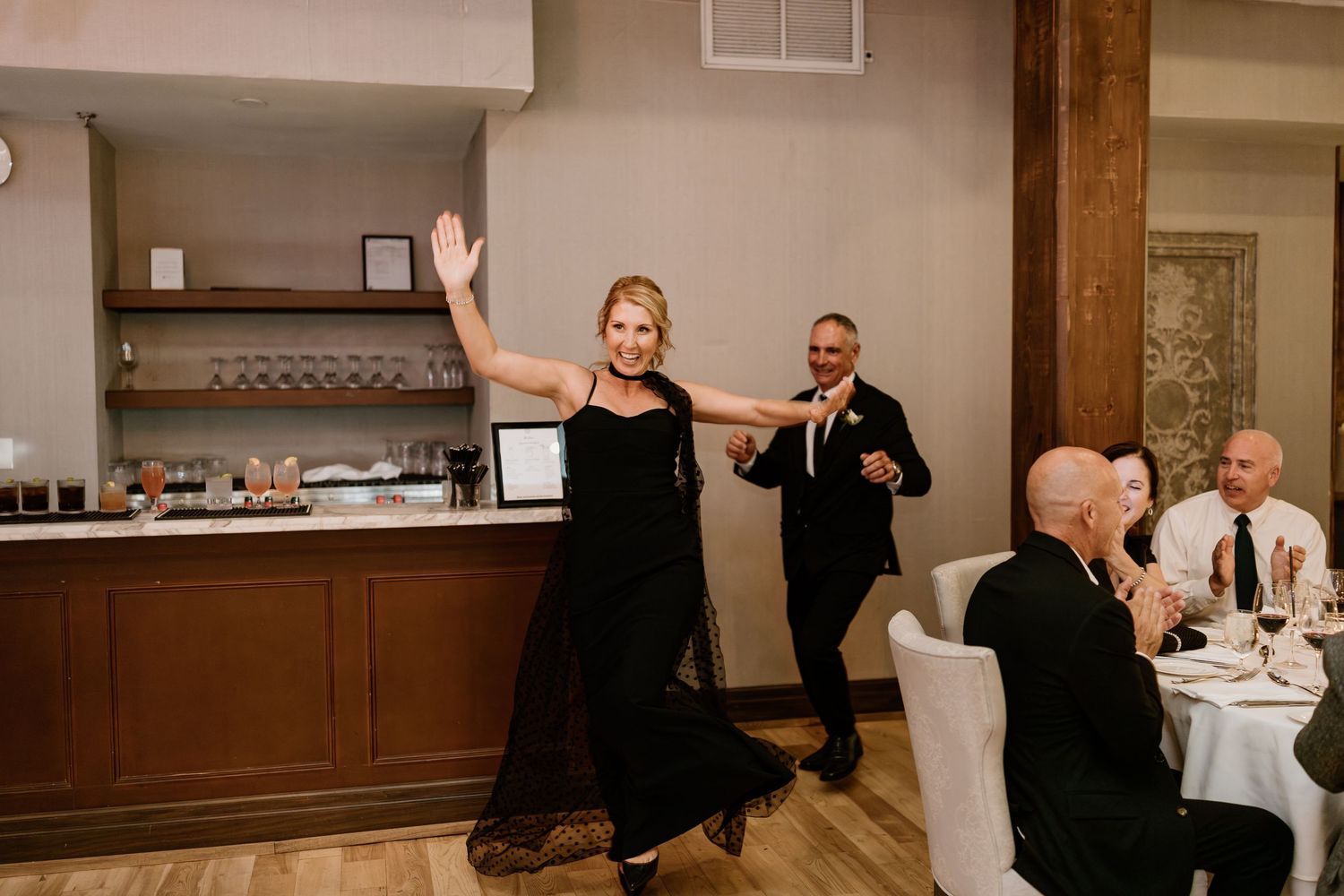 Wedding guests dancing and celebrating in a rustic reception venue with wooden beams and stone walls.
