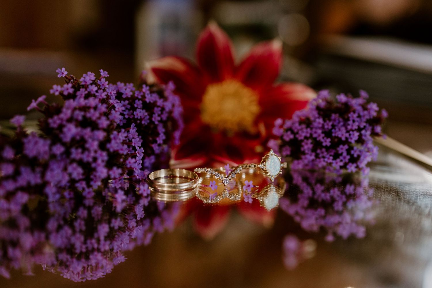 Wedding rings and purple flowers arranged in artistic detail shot.