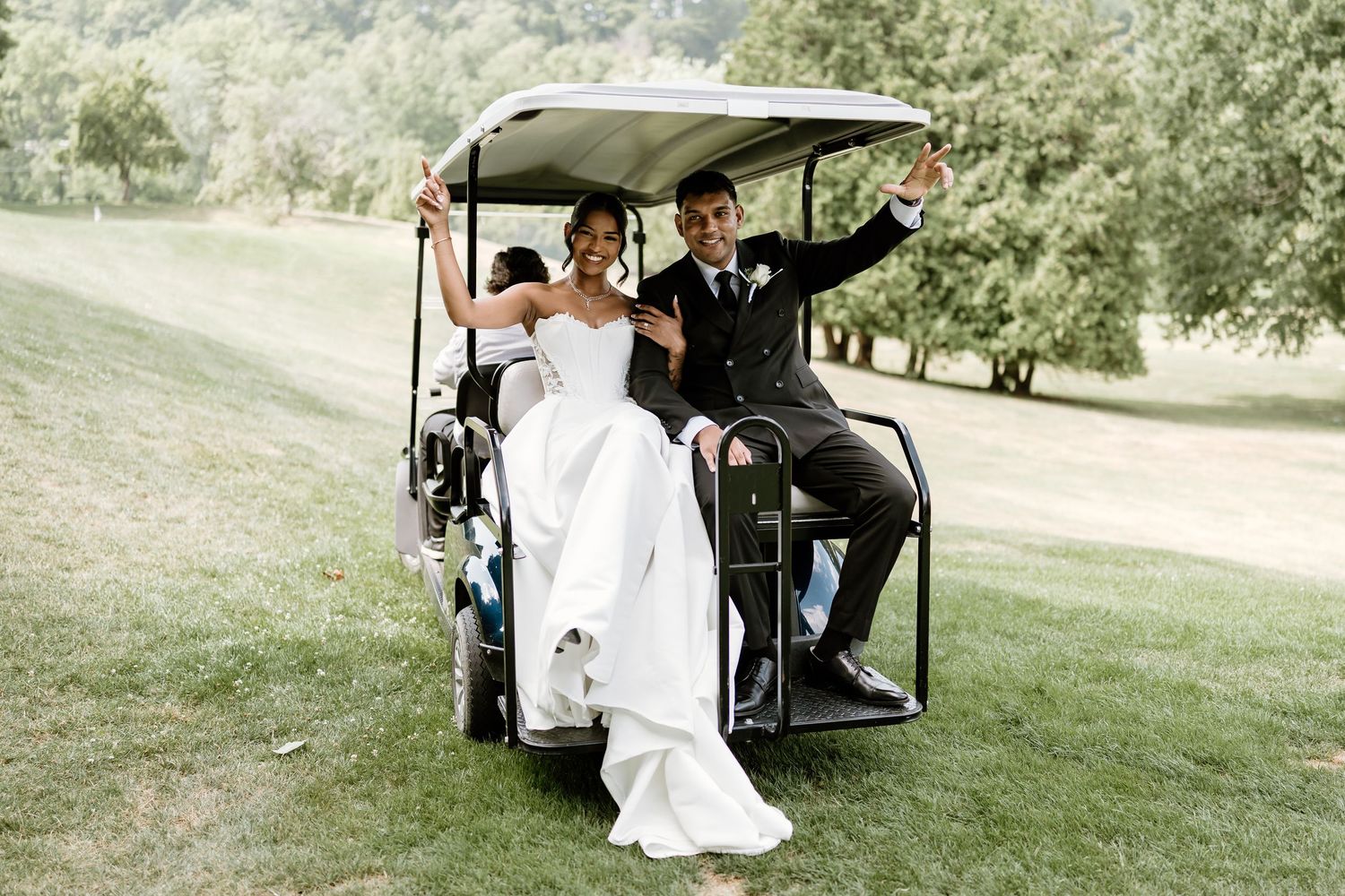 Newlyweds riding in a golf cart during their outdoor wedding celebration.