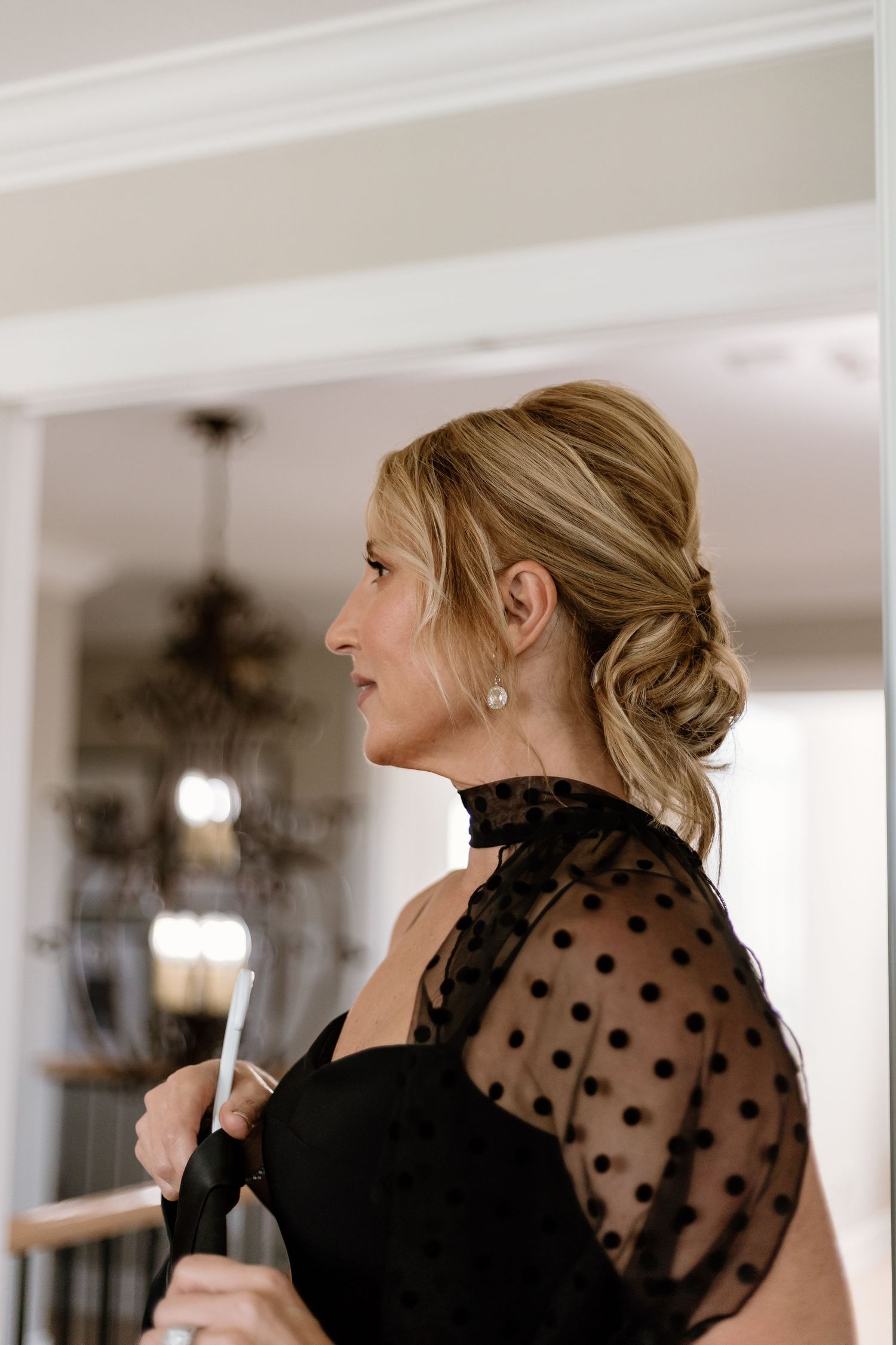 Side profile of person wearing black polka dot sheer sleeve dress with elegant updo hairstyle.
