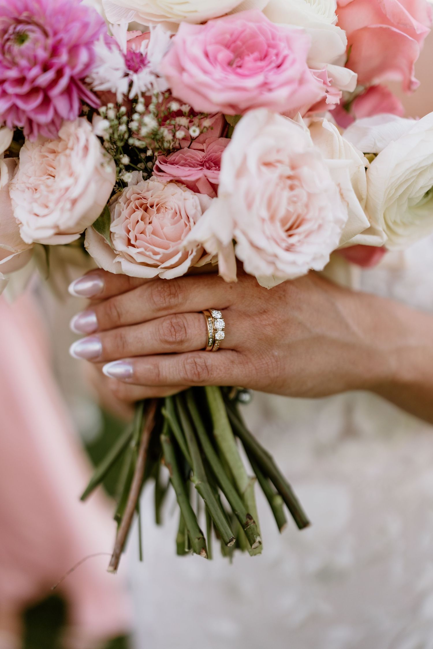 Bride holding a pink and white rose wedding bouquet with a diamond engagement ring on her finger.