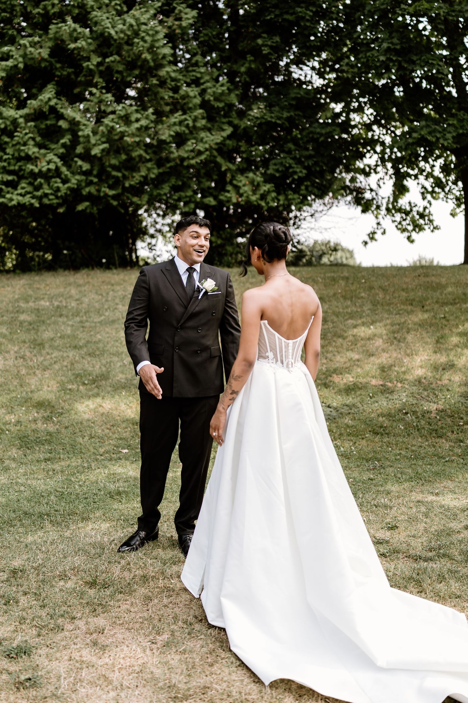 Couple in wedding attire sharing a moment on a scenic grassy hillside.