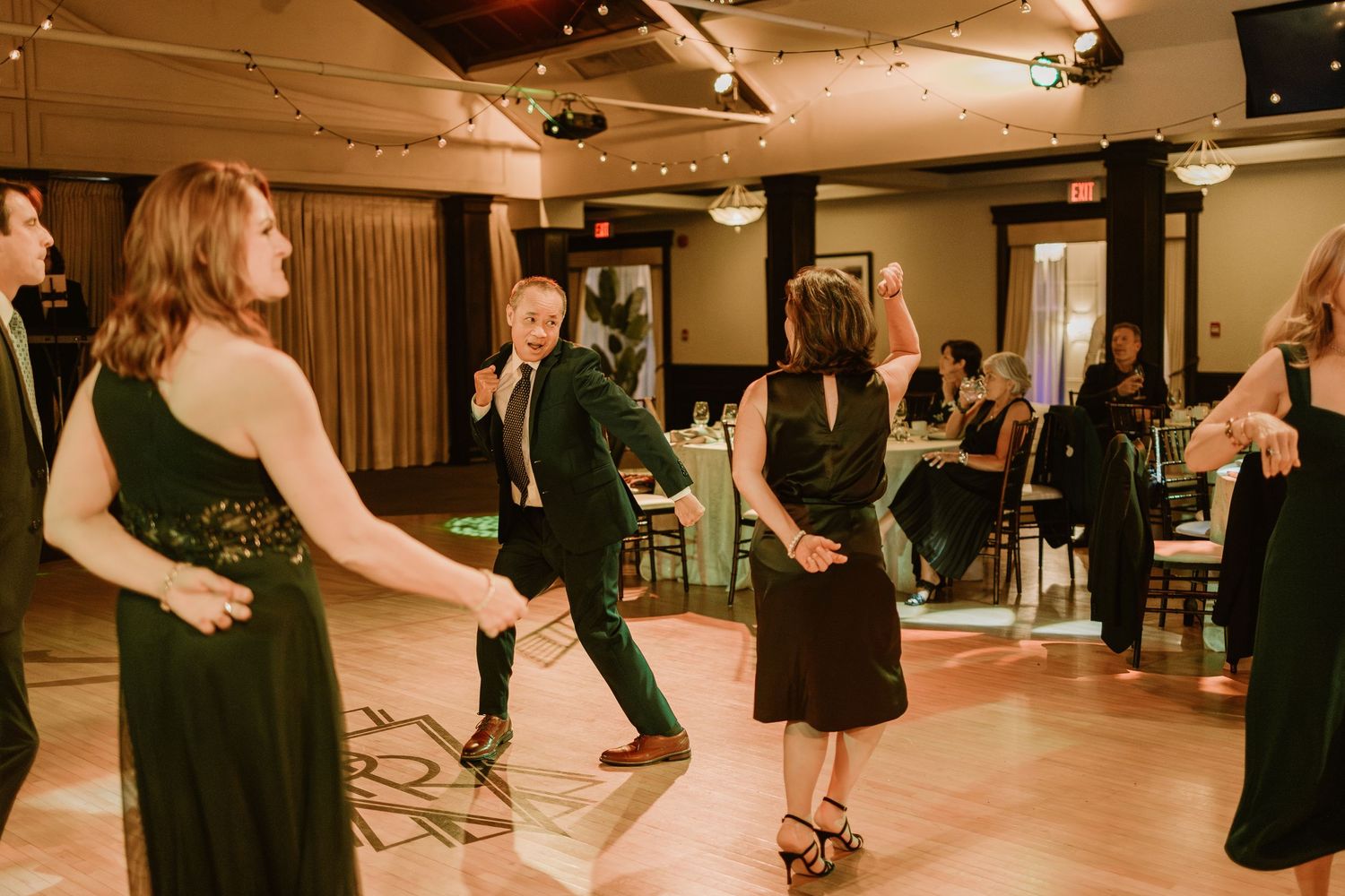 Guests dancing together at an indoor wedding reception with warm lighting and dark decor.