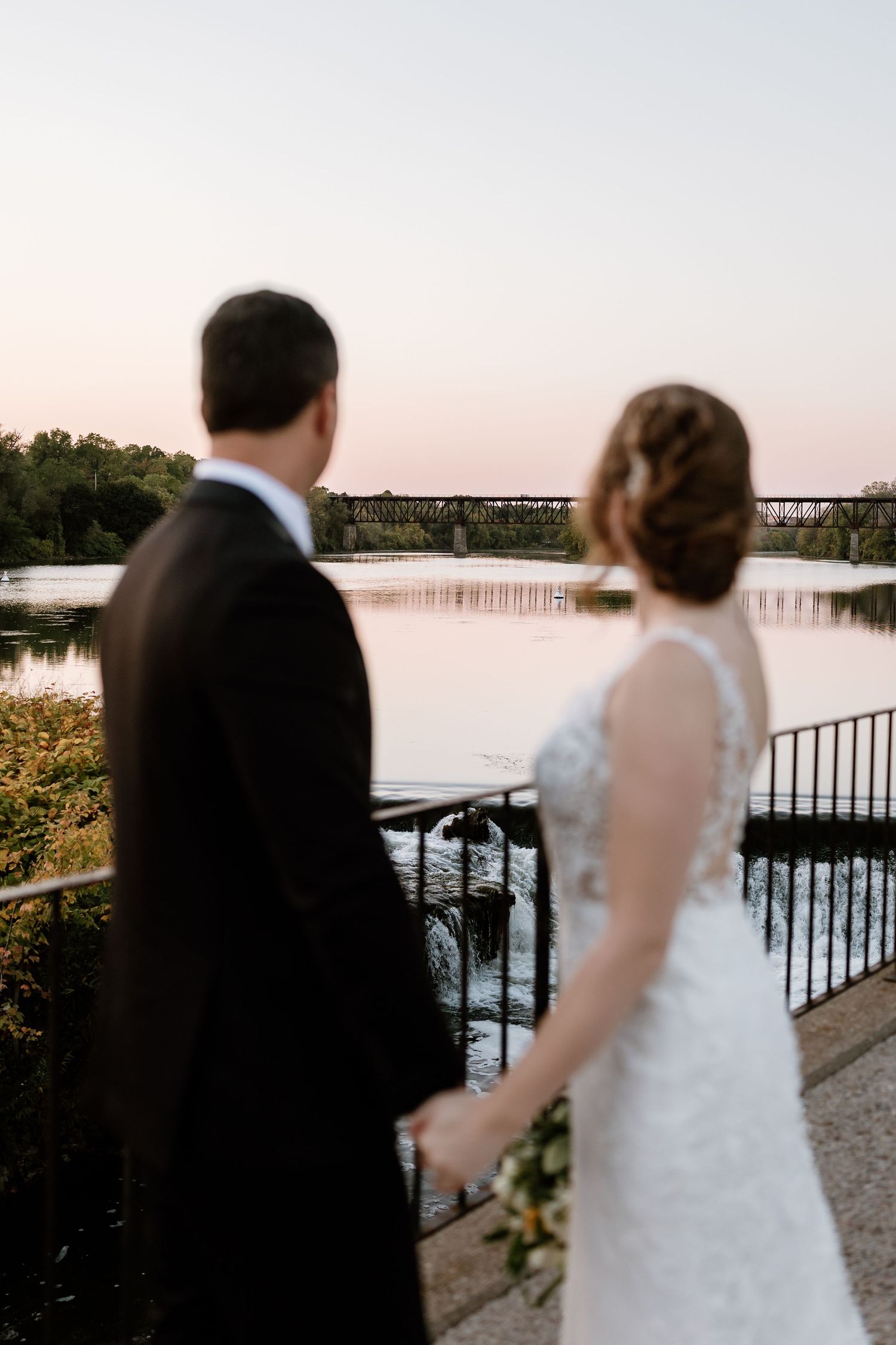 Silhouetted couple admires sunset view over lake from stone pavilion.