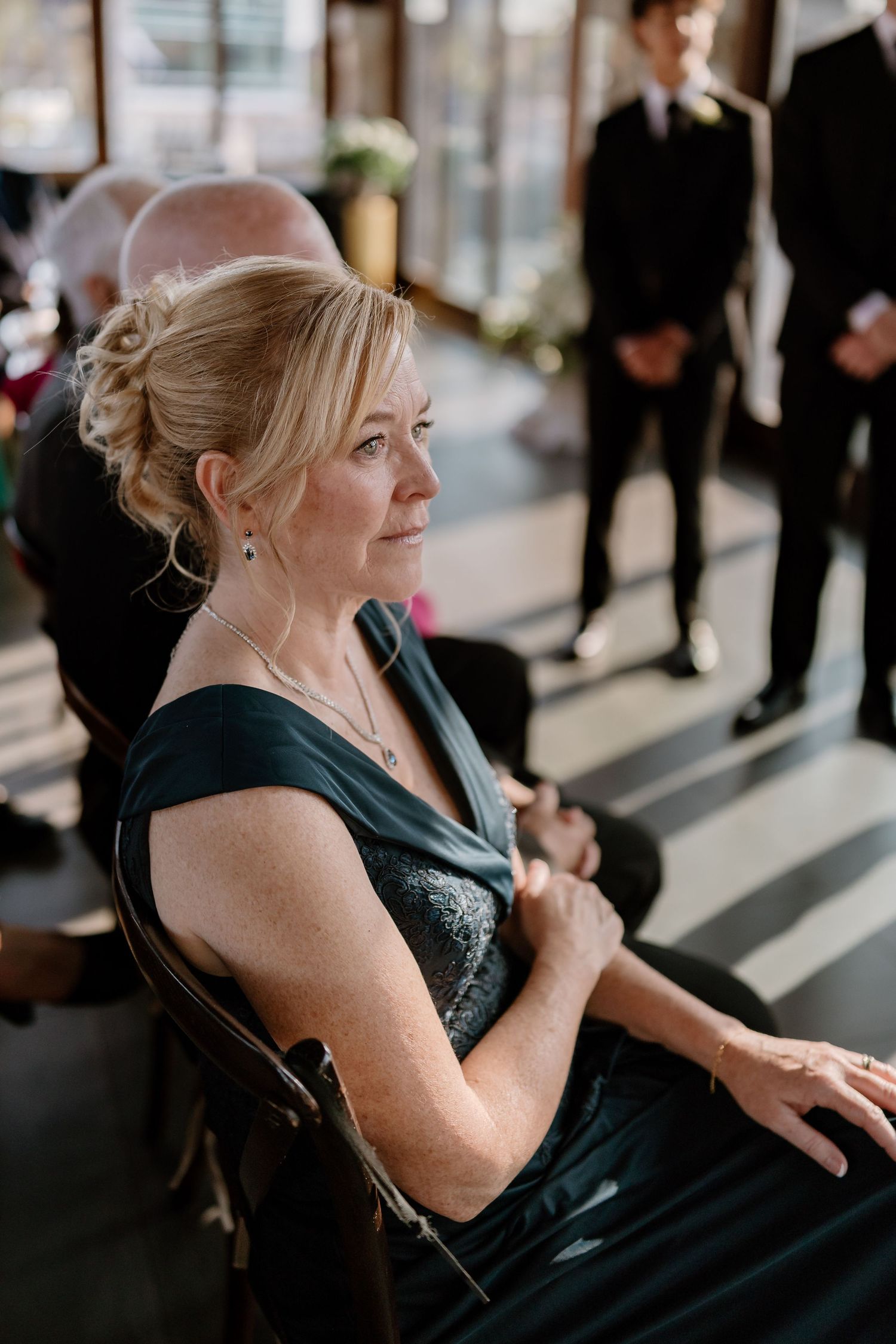 Wedding guest in a black dress sits by a window during an elegant event.