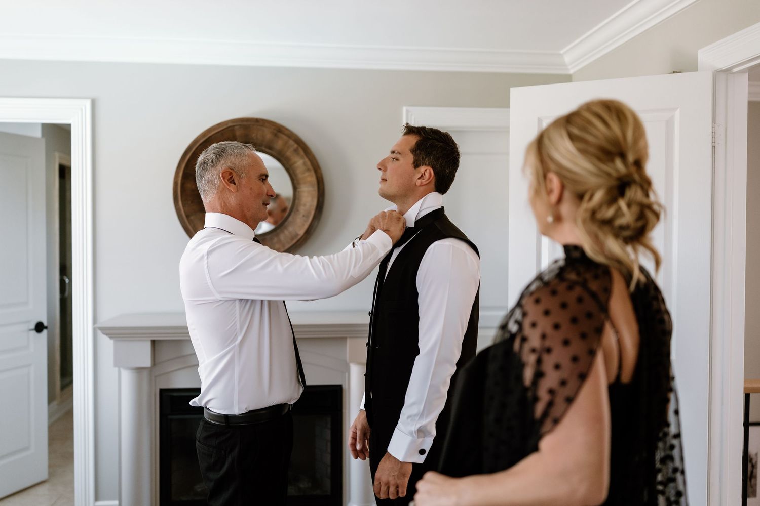 Wedding preparation scene showing formal attire adjustments in bright interior setting.