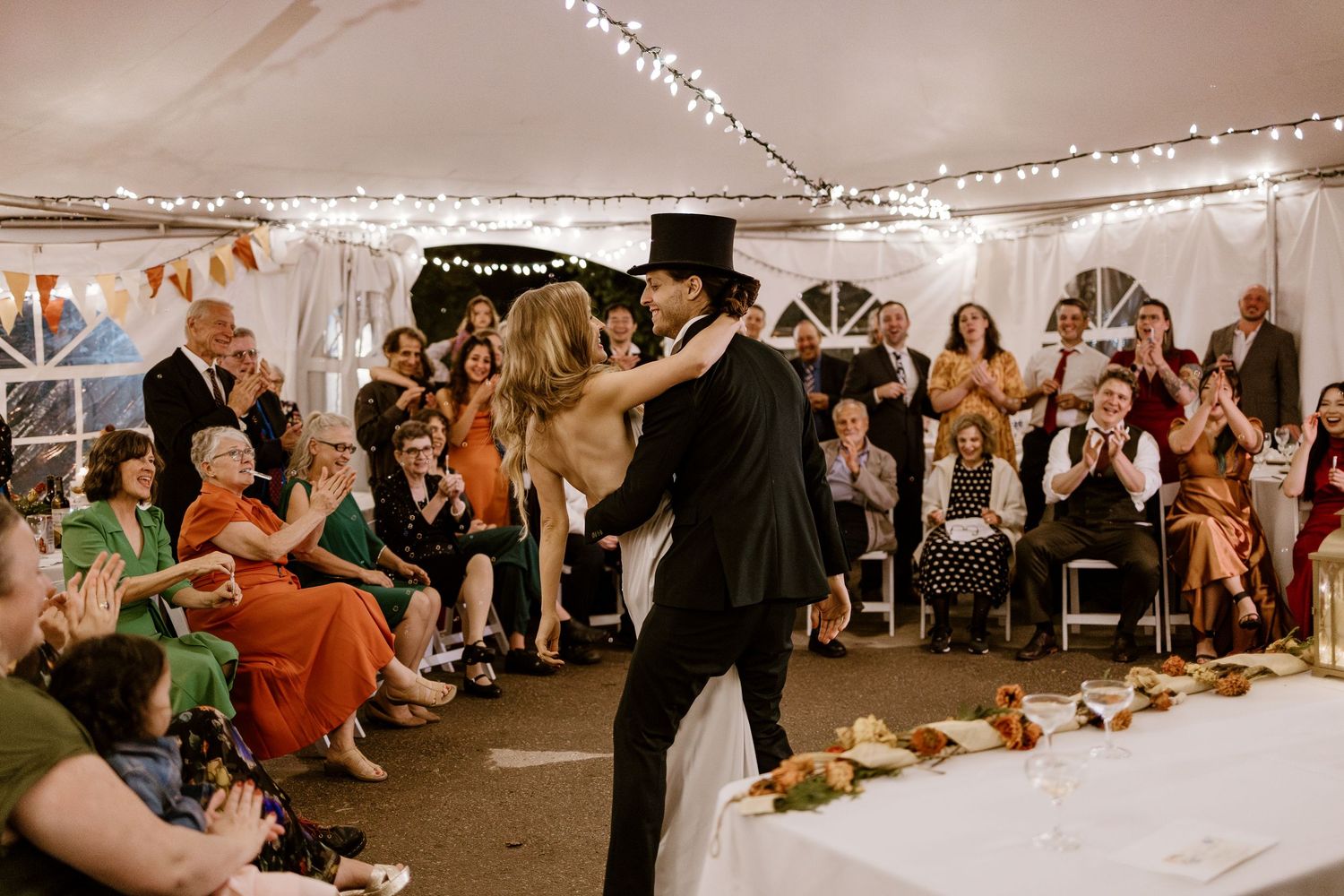 Wedding reception dance scene with guests watching under string lights in a tent.
