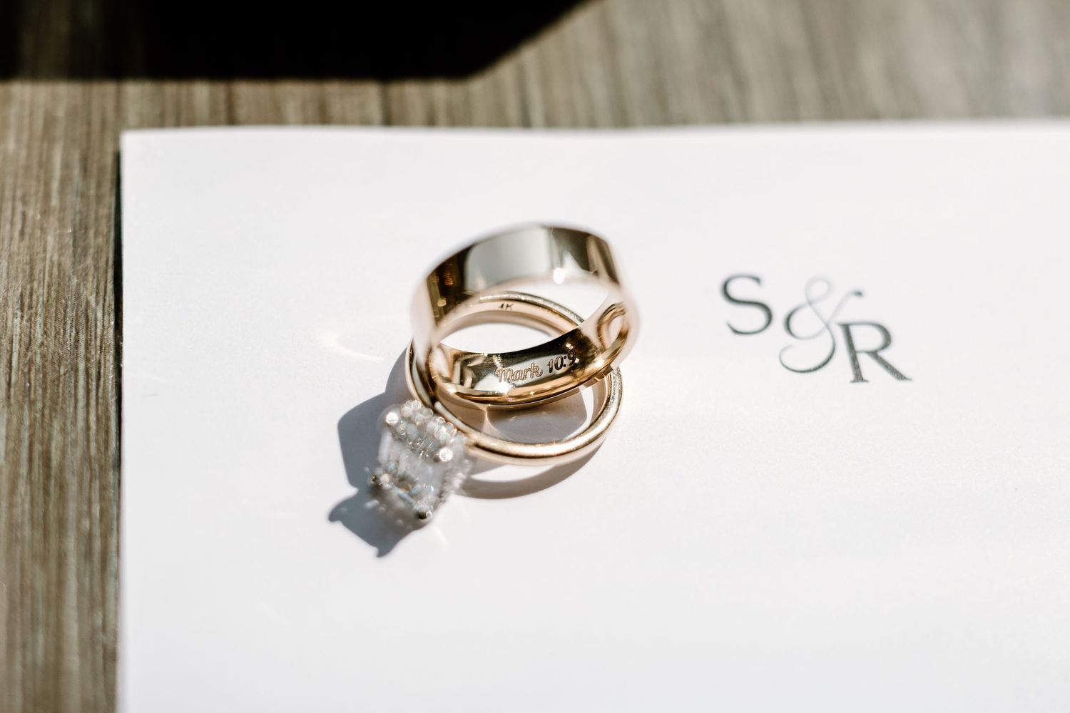 Wedding rings casting shadows on white paper with elegant text detail.