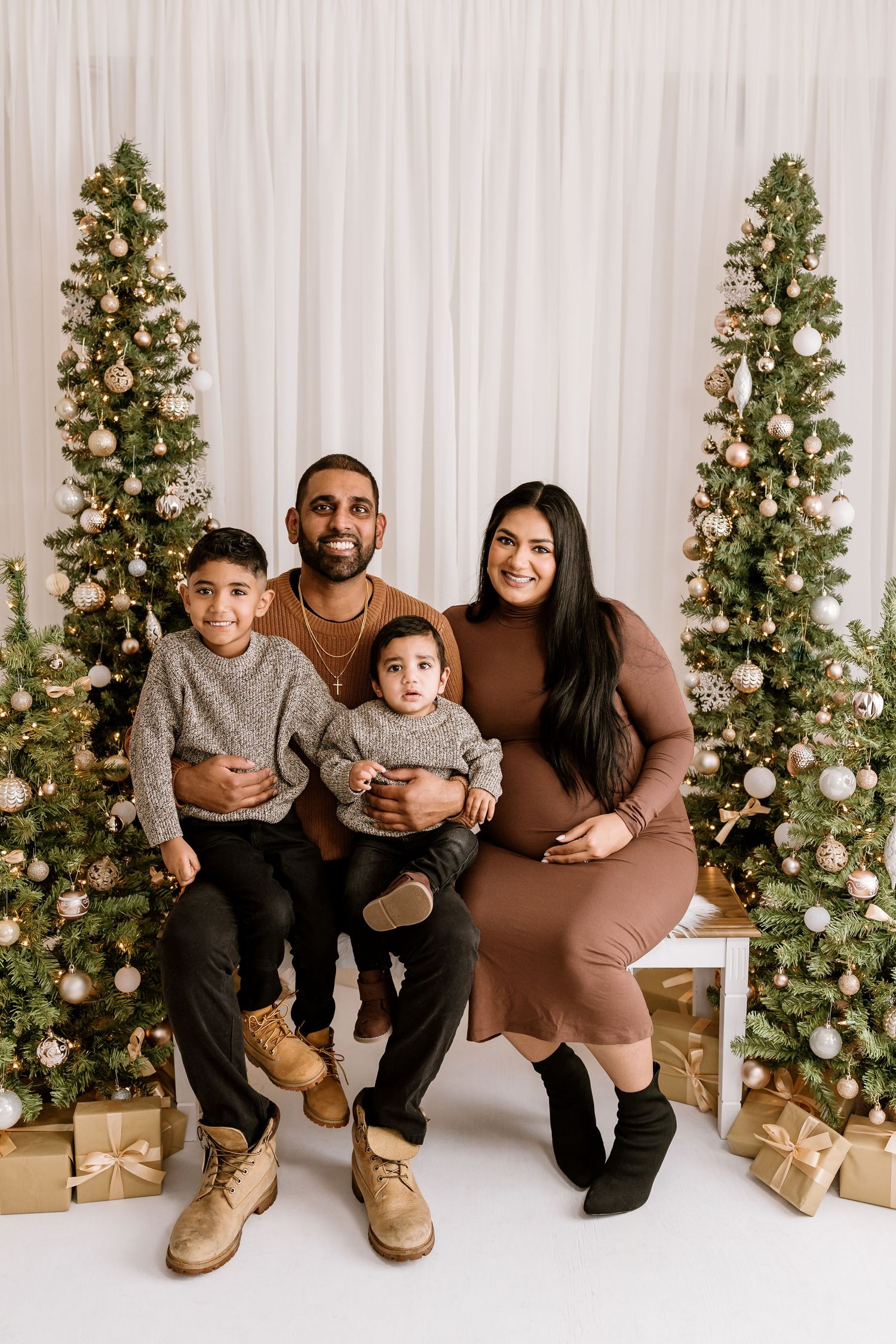 Family portrait with Christmas trees and gold wrapped presents in a festive holiday setting.