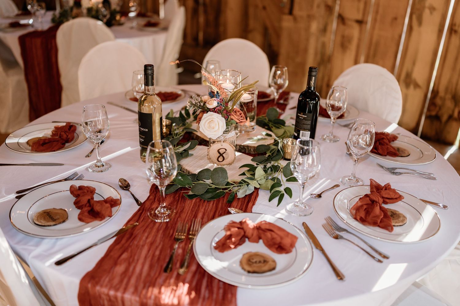 Formal place settings with red accents and wine glasses at wedding reception.