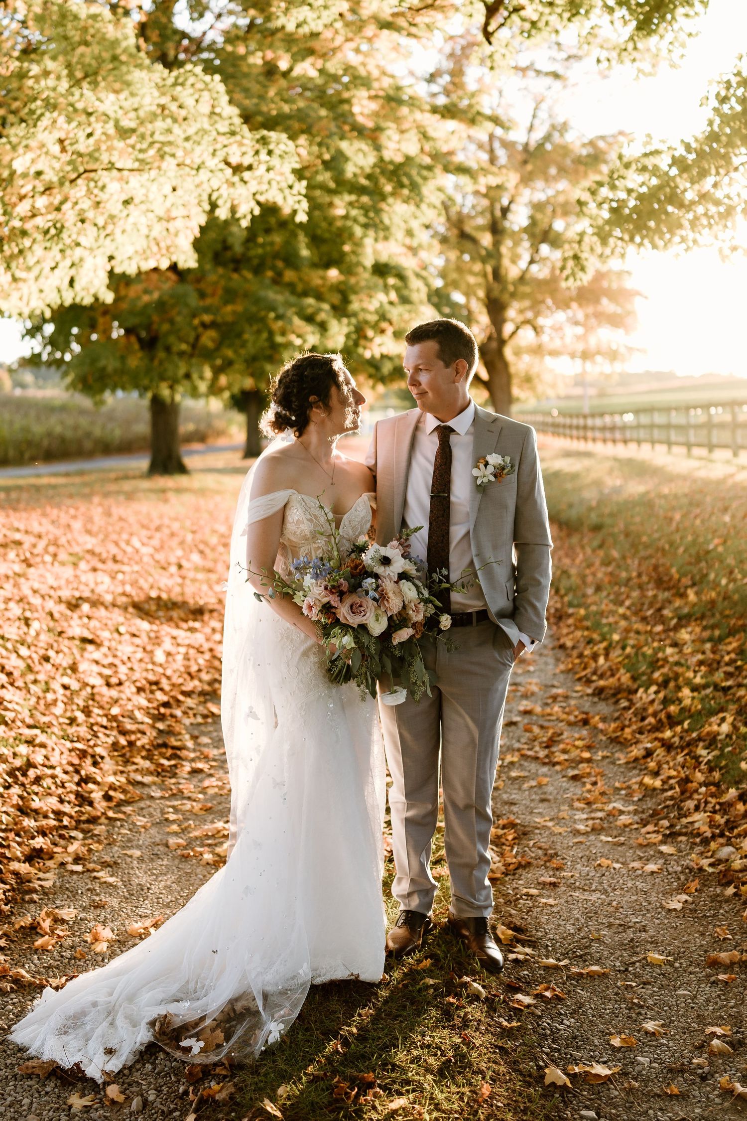 Autumn wedding scene with couple walking through fallen leaves at sunset.