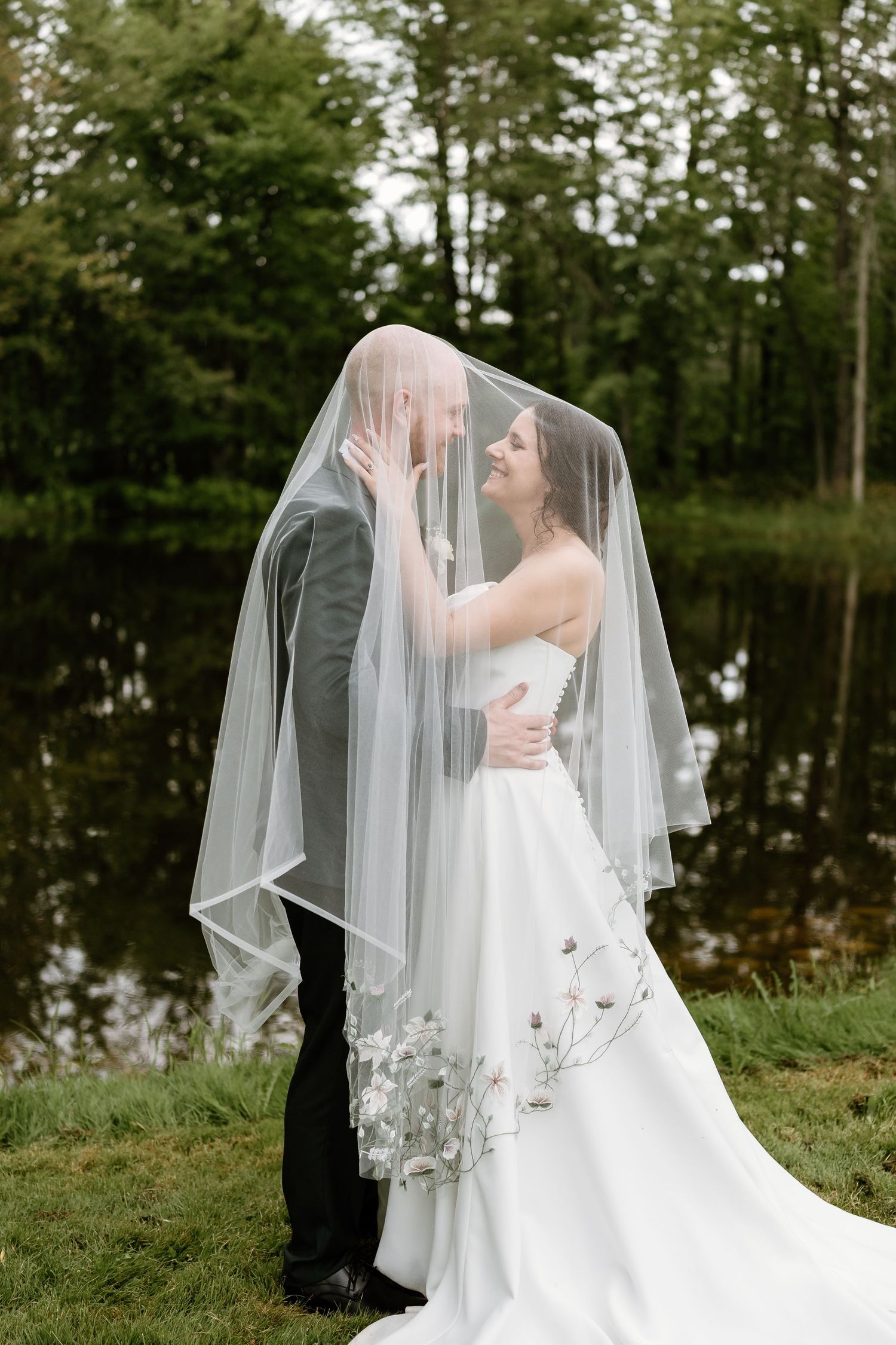 Intimate moment under wedding veil with lake and forest backdrop.