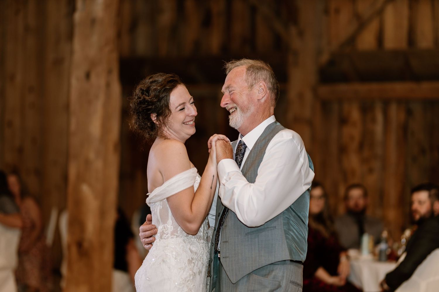 Wedding guests dancing and celebrating on a wooden floor under string lights in a rustic barn setting.