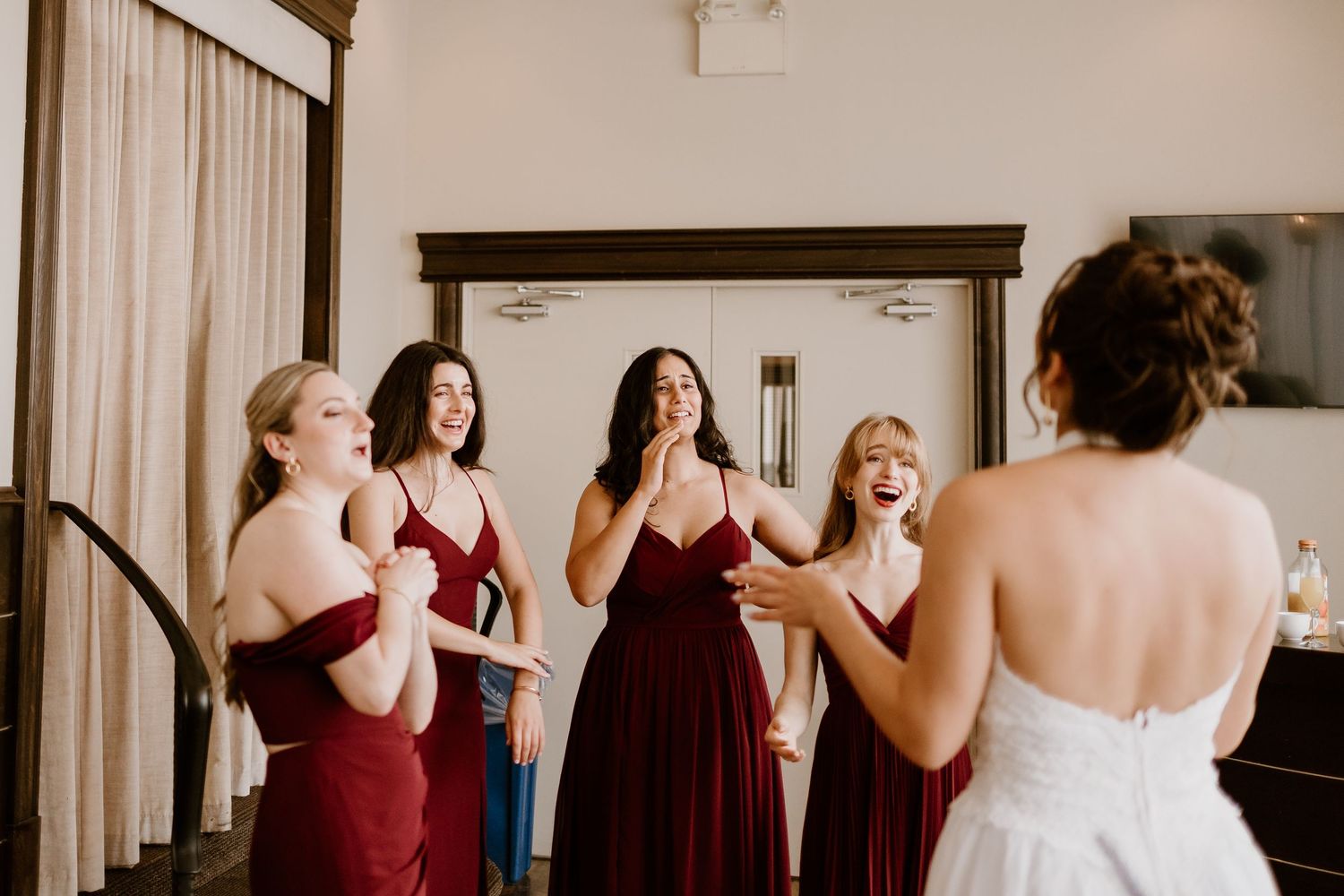 Wedding party in burgundy dresses and white gown gather together in an elegant room.